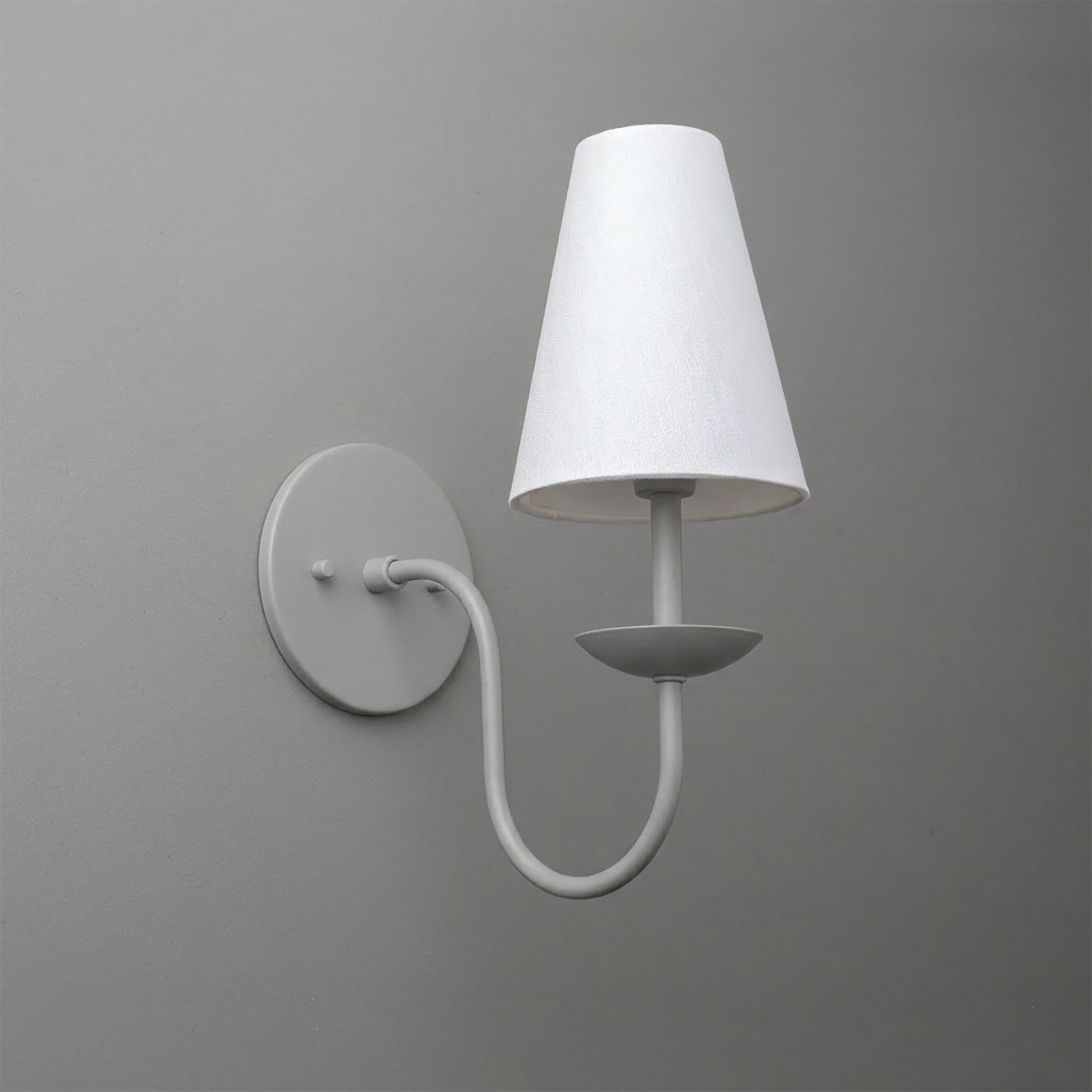 White metal wall sconce with round base and curved arm holding a fabric tapered lampshade. - SCONCE MODEL NO. 7085