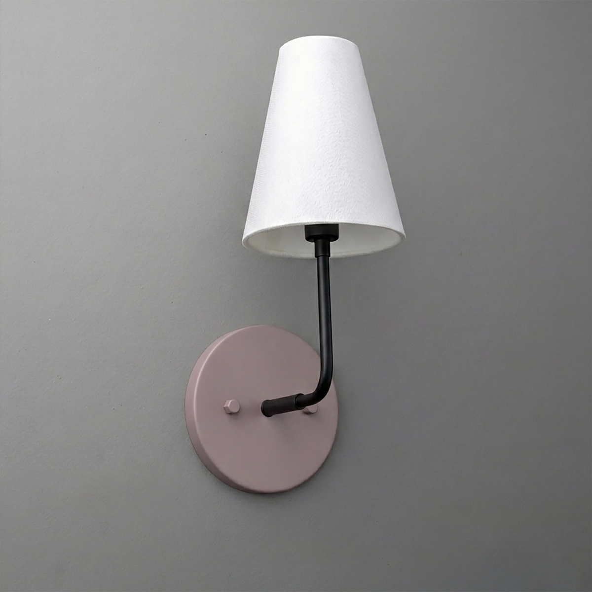 Wall sconce with a round muted pink metal base, black arm, and white tapered fabric lampshade. - SCONCE MODEL NO. 3928