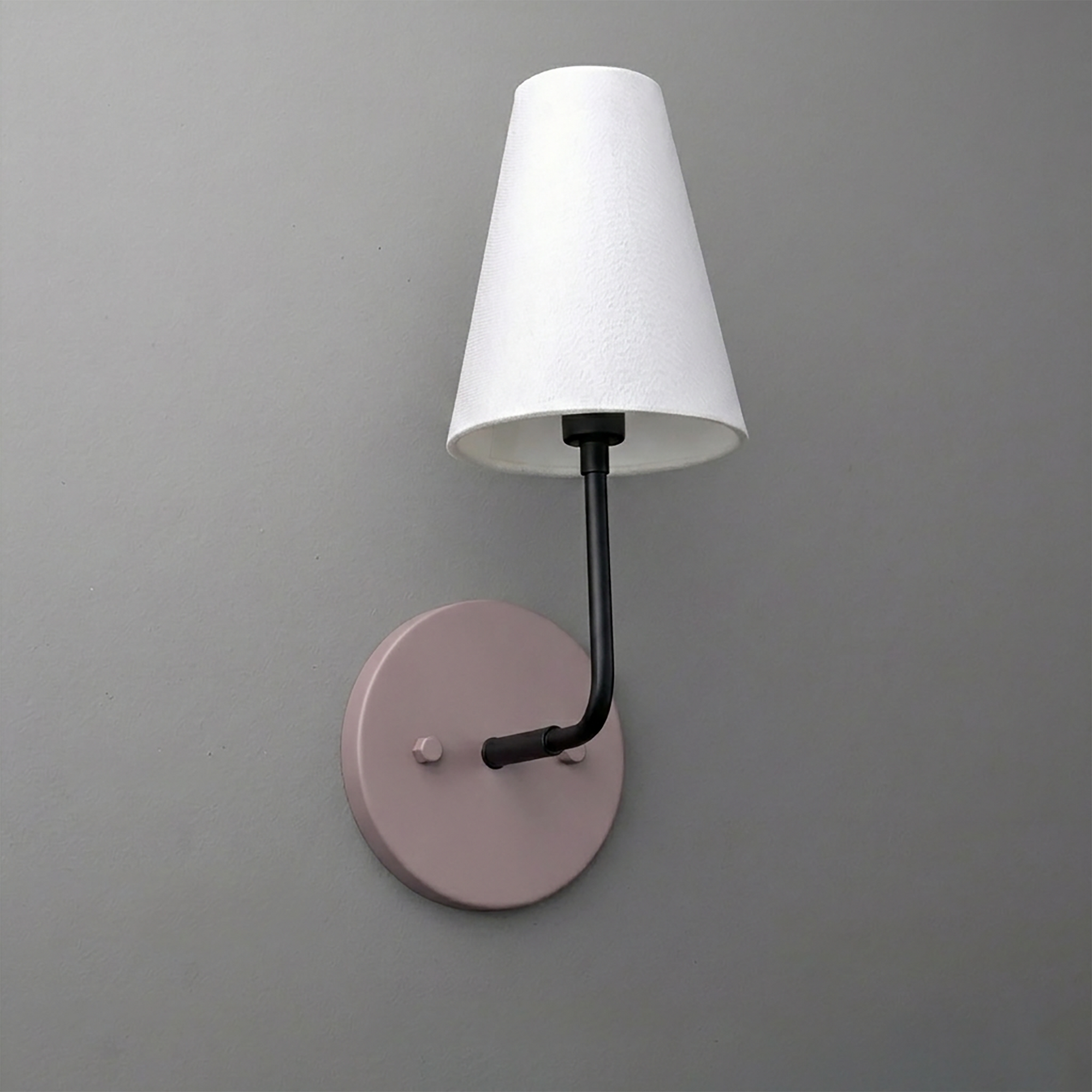 Wall sconce with a round muted pink metal base, black arm, and white tapered fabric lampshade. - SCONCE MODEL NO. 3928