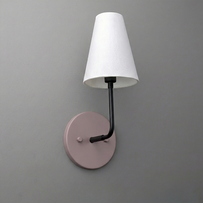 Wall sconce with a round muted pink metal base, black arm, and white tapered fabric lampshade. - SCONCE MODEL NO. 3928
