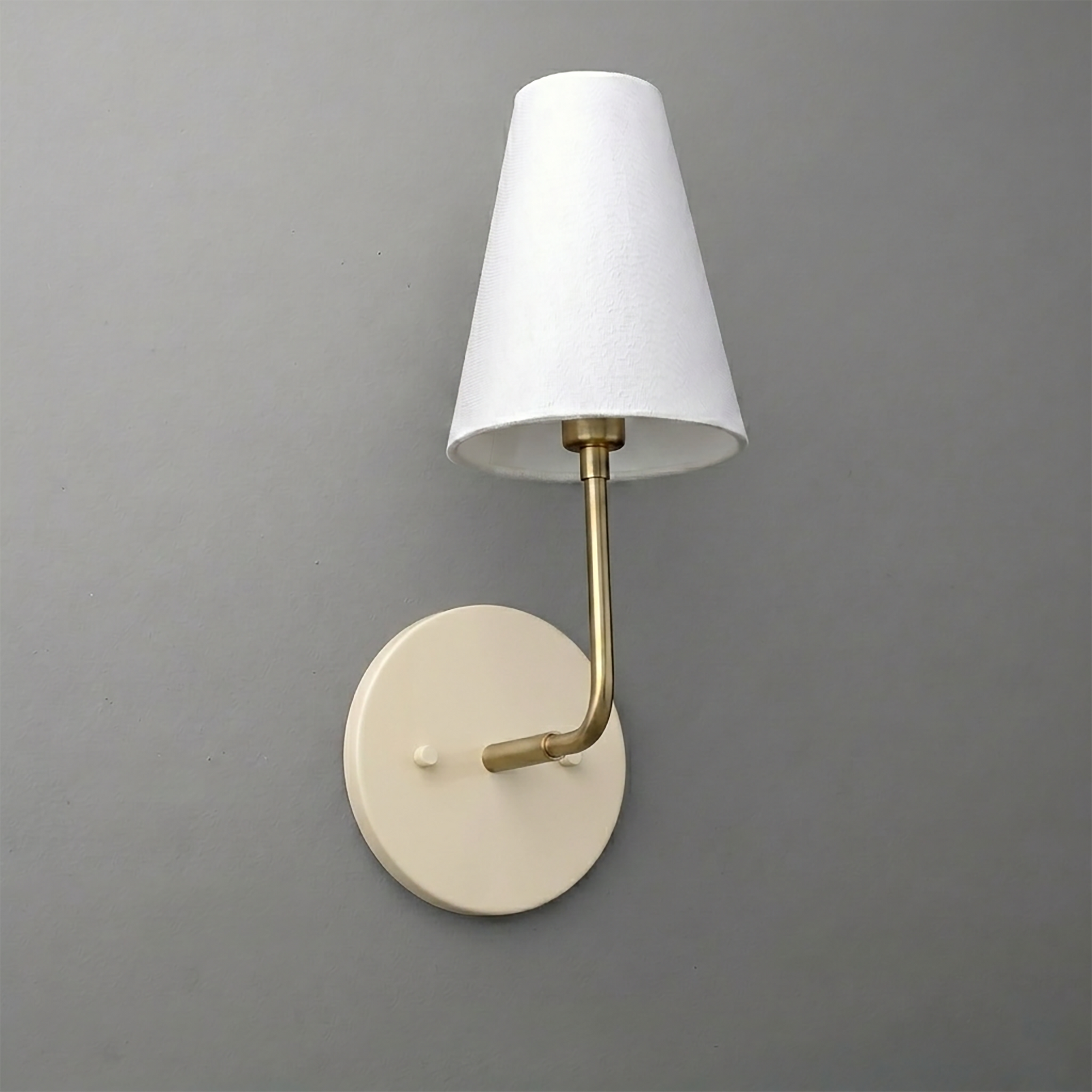 Wall sconce with round beige metal base, brass arm, and white tapered fabric lampshade. - SCONCE MODEL NO. 3928