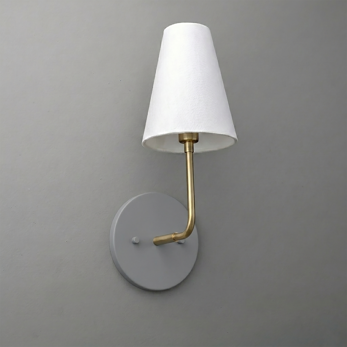 Wall-mounted sconce with round gray base, brass arm, and white tapered fabric shade. - SCONCE MODEL NO. 3928