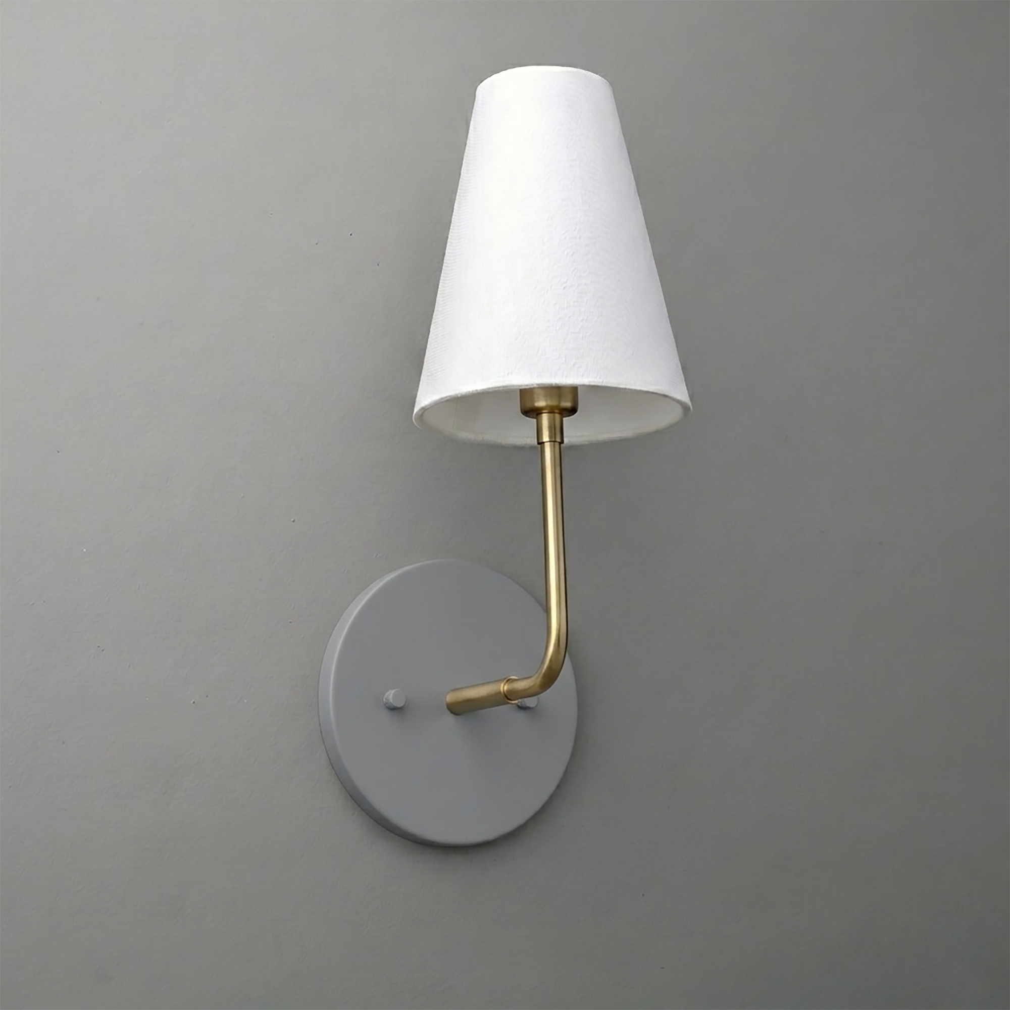 Wall-mounted sconce with round gray base, brass arm, and white tapered fabric shade. - SCONCE MODEL NO. 3928
