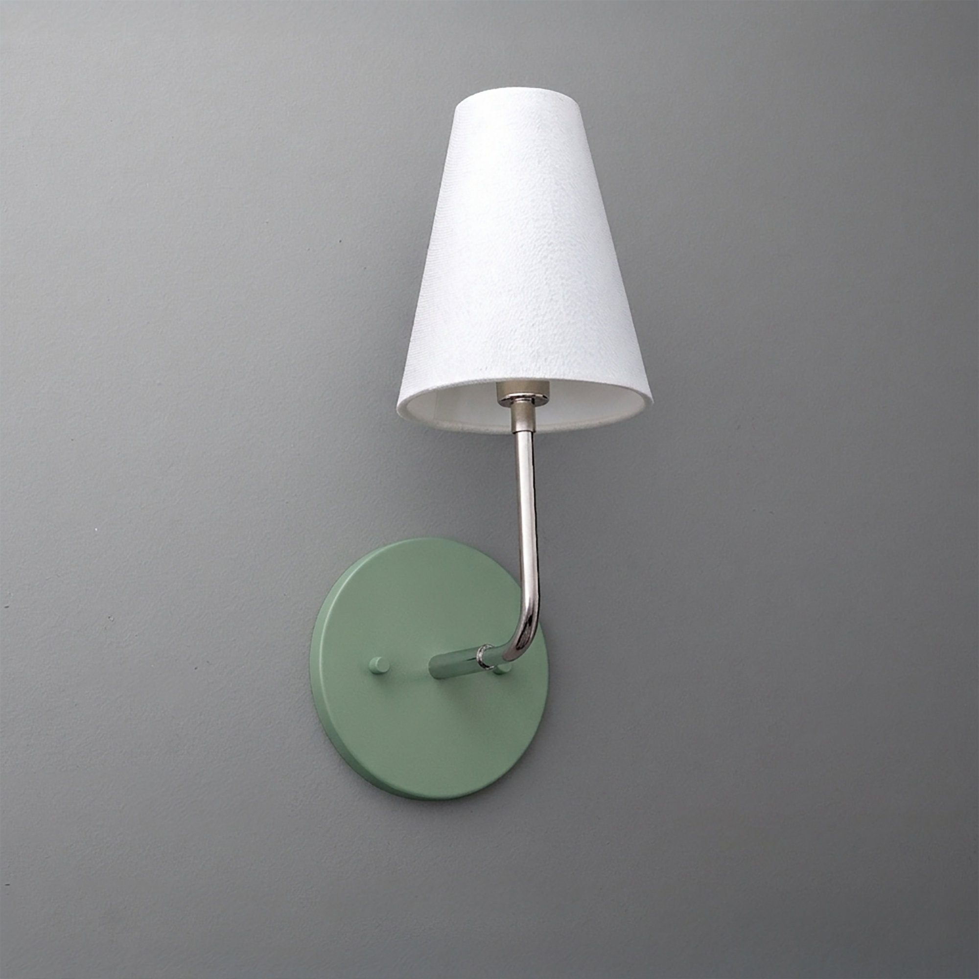 Wall-mounted sconce with round sage green metal base and slender silver arm holding a white tapered fabric shade. - SCONCE MODEL NO. 3928