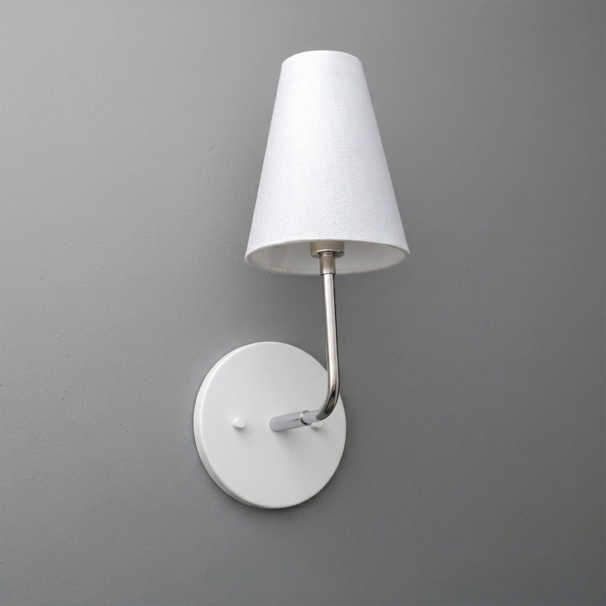 White metal wall sconce with round base and straight arm holding a tapered white fabric shade. - SCONCE MODEL NO. 3928