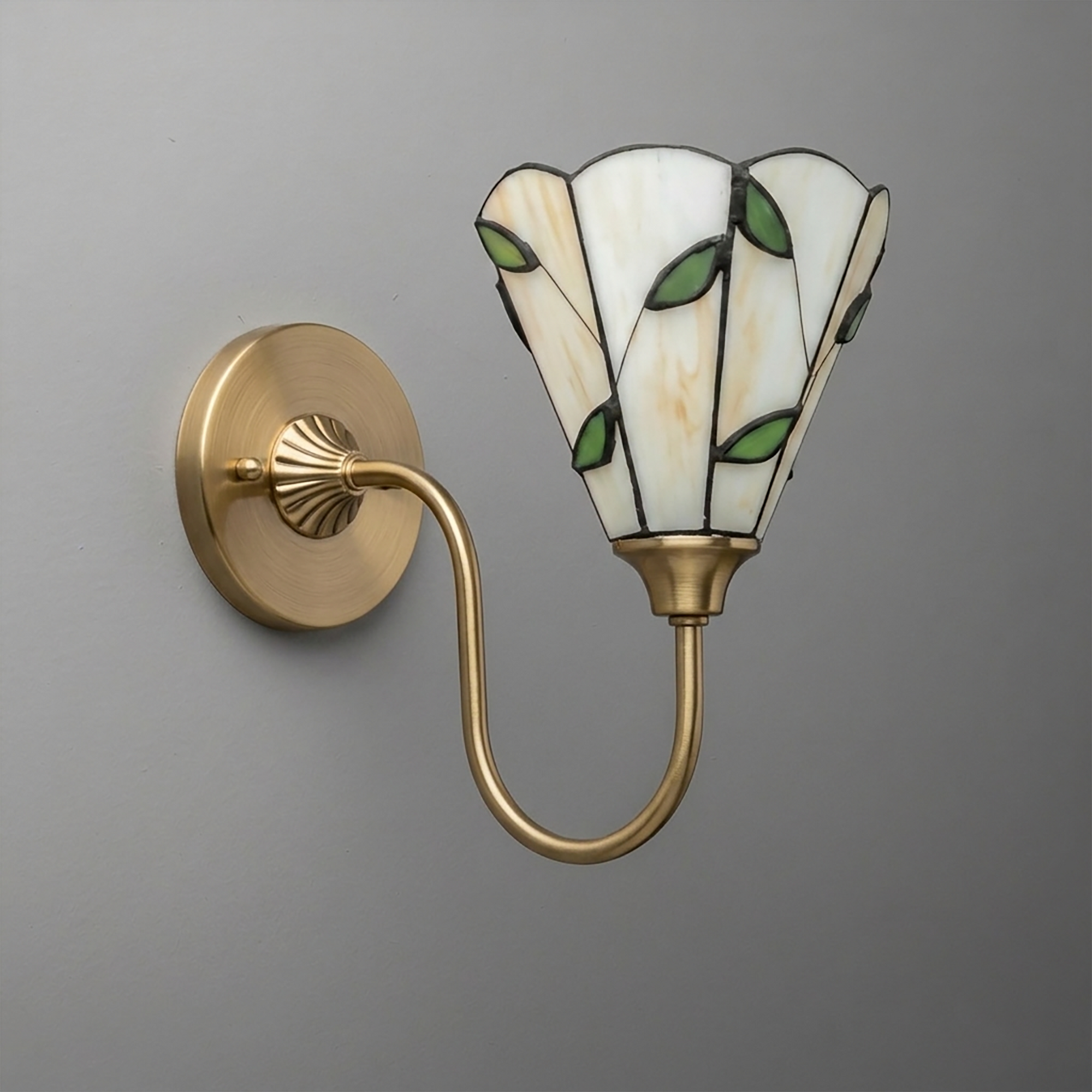 Brushed brass wall sconce with curved arm and stained glass shade featuring white panels and green leaf accents. - SCONCE MODEL NO. 1053
