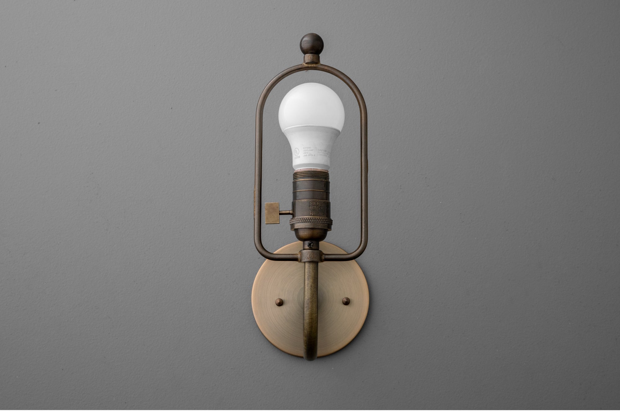 Antique brass wall sconce with exposed bulb and rounded rectangular frame on gray background. - SCONCE MODEL NO. 0303
