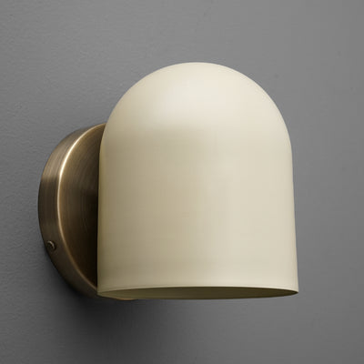Antique brass wall sconce with smooth cream glass shade mounted on gray wall. - SCONCE MODEL NO. 2424