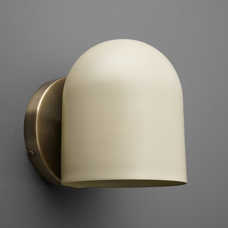Antique brass wall sconce with smooth cream glass shade mounted on gray wall. - SCONCE MODEL NO. 2424