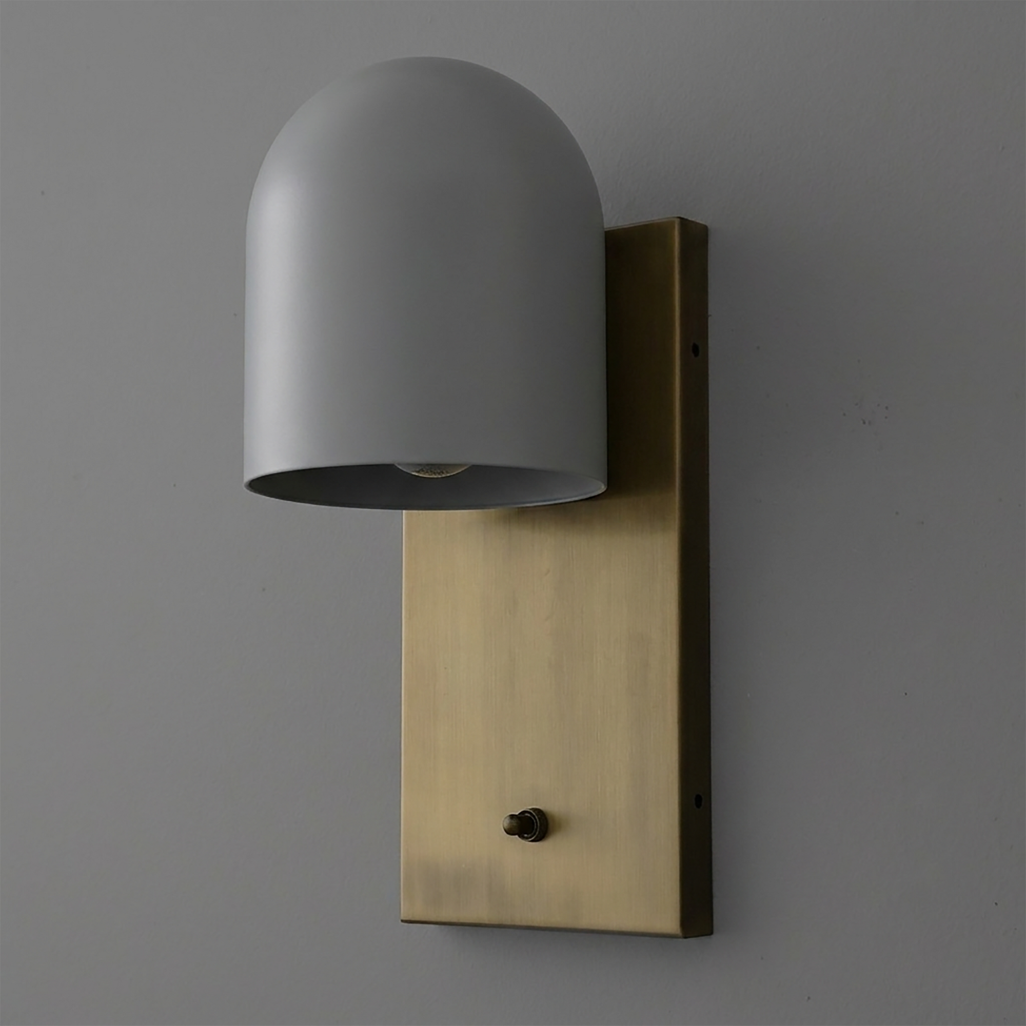 Matte gray dome-shaped metal sconce with single bulb mounted on a rectangular brushed brass backplate with a small black. - SCONCE MODEL NO. 6029