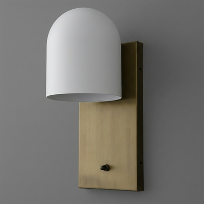 Matte white dome-shaped glass shade on a vertical brushed brass rectangular backplate wall sconce with a small black switch. - SCONCE MODEL NO. 6029
