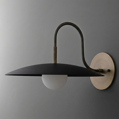 Black metal disc-shaped sconce with curved brass arm and frosted globe bulb shade on round brass wall plate. - SCONCE MODEL NO. 9171