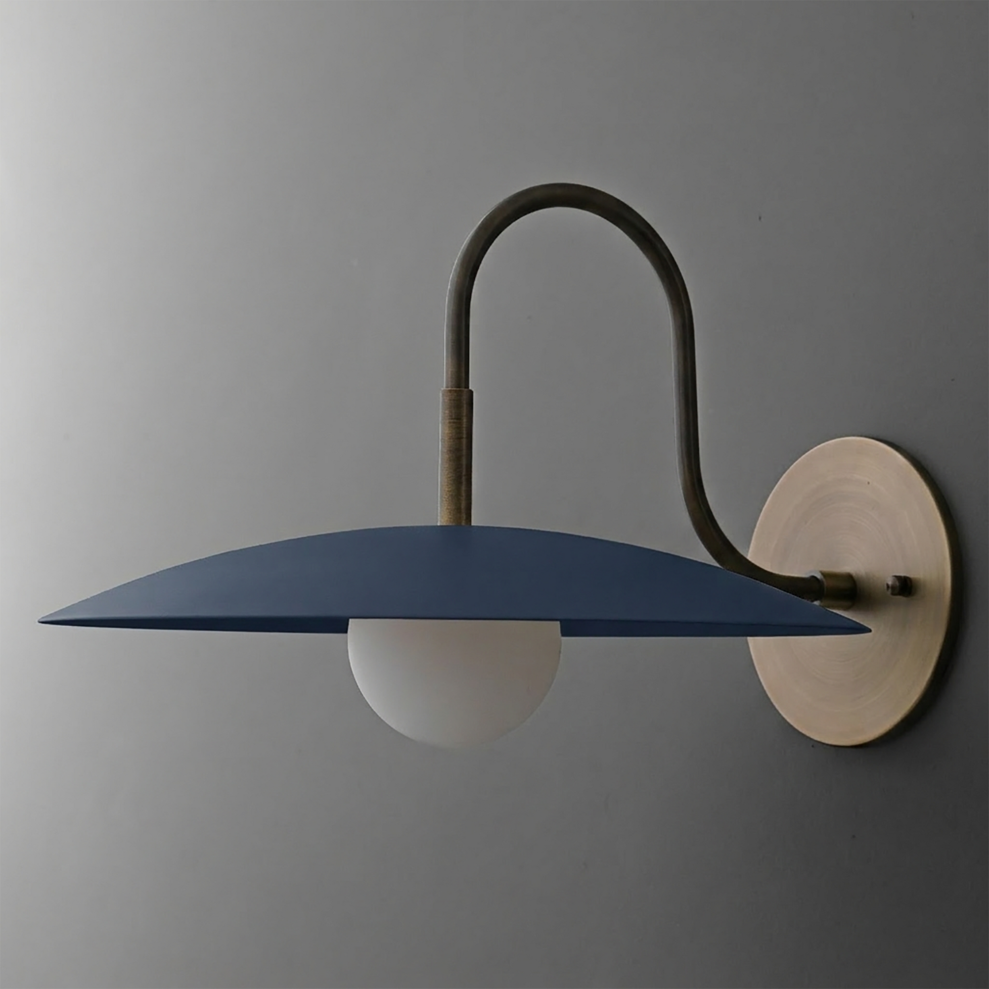 Wall sconce with matte navy blue disc shade, frosted globe bulb, and brass curved arm on round brass base. - SCONCE MODEL NO. 9171