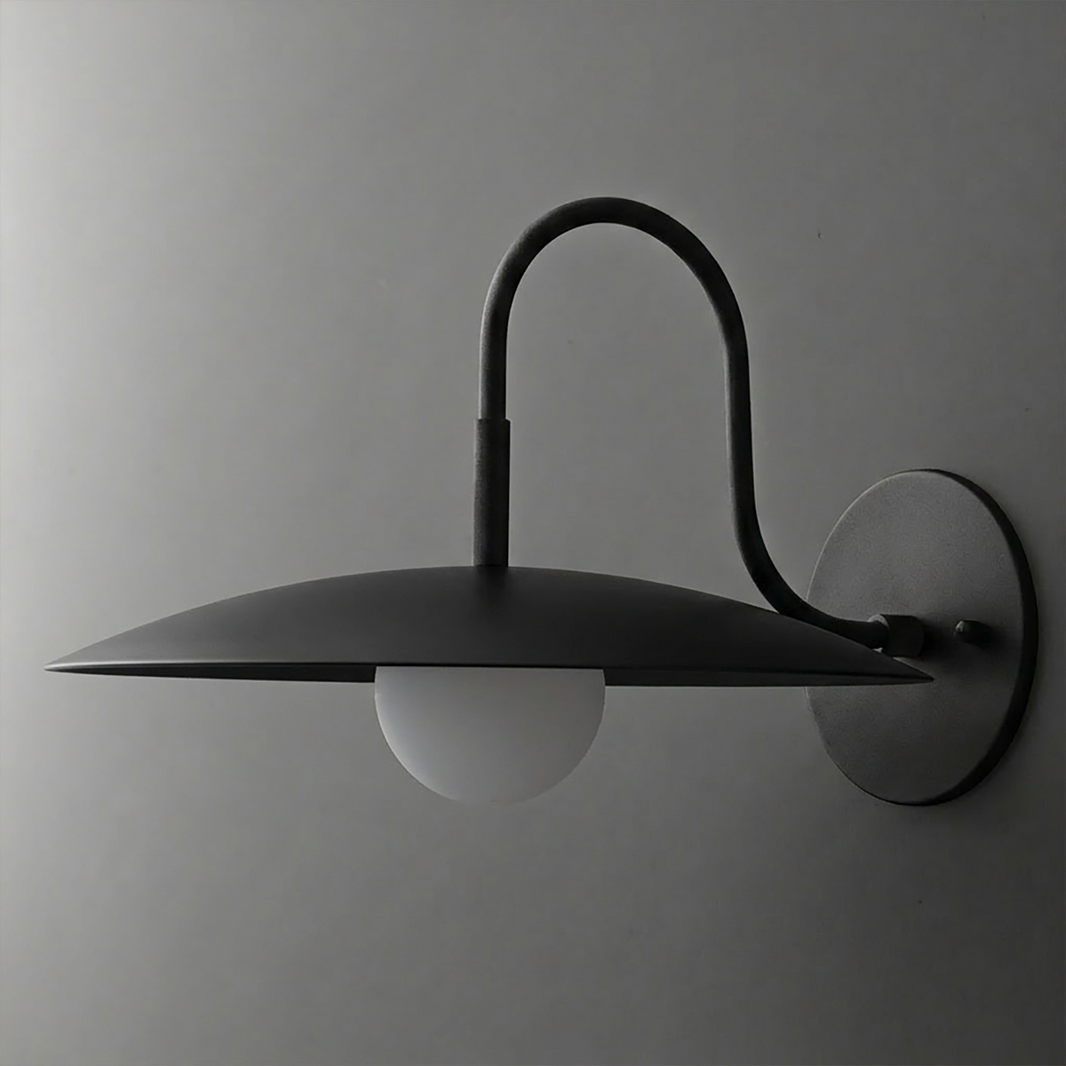 Black metal wall sconce with curved arm and wide, flat disc shade over a white globe bulb. - SCONCE MODEL NO. 9171