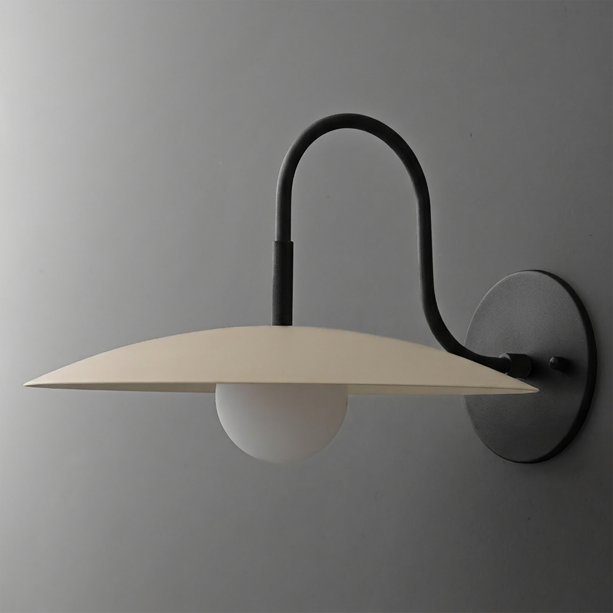 Black metal wall sconce with curved arm and flat beige shade over a white globe bulb. - SCONCE MODEL NO. 9171