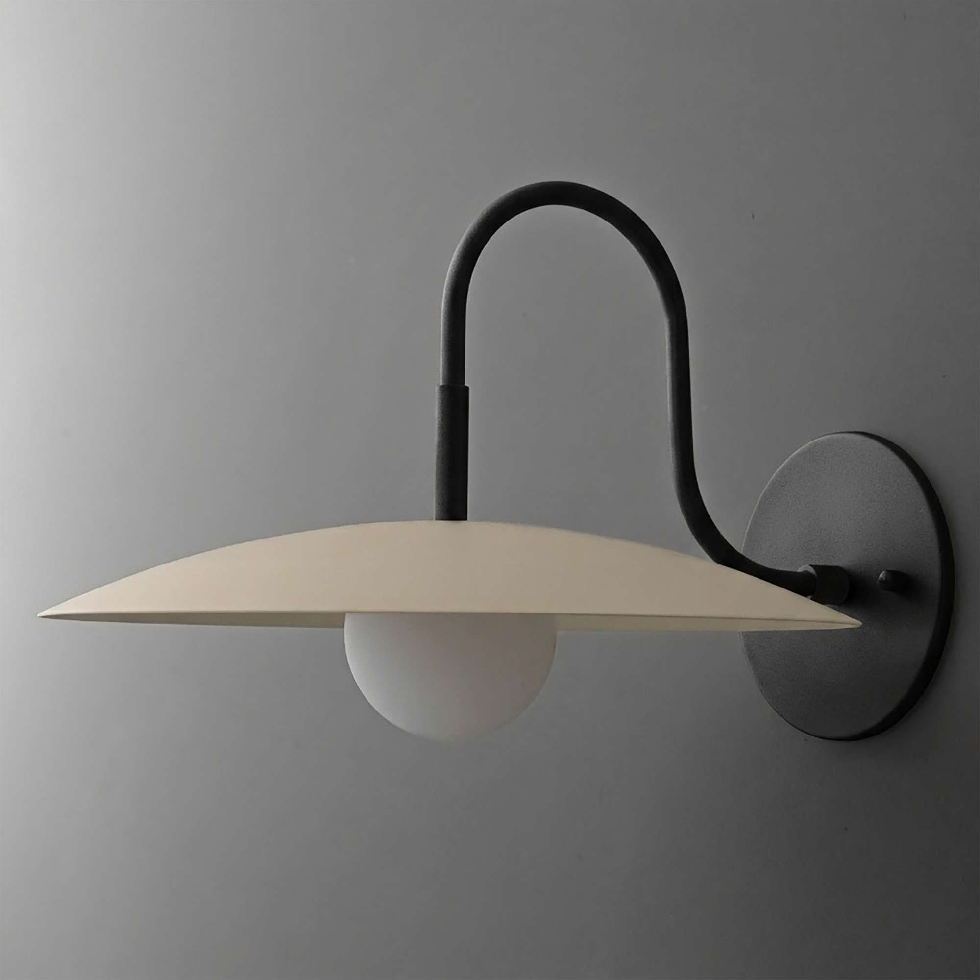 Black metal wall sconce with curved arm and flat beige shade over a white globe bulb. - SCONCE MODEL NO. 9171
