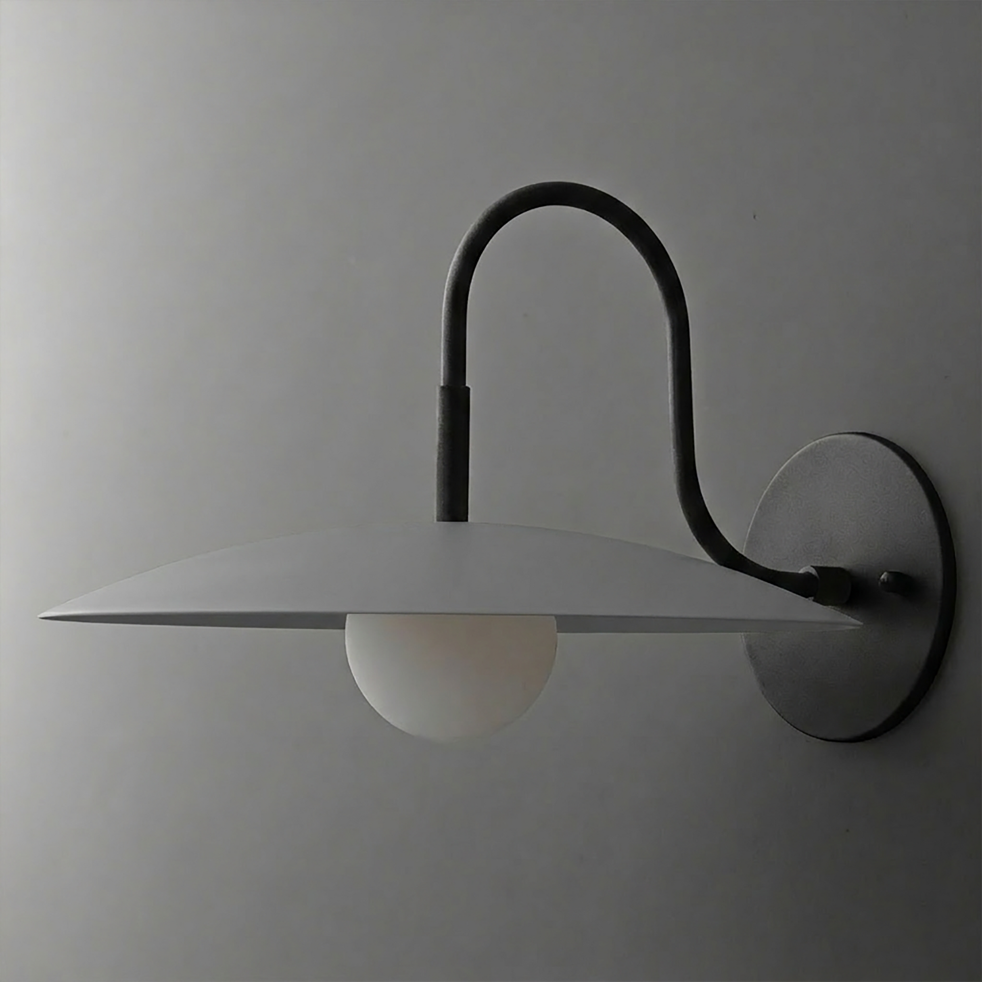Matte black metal wall sconce with a curved arm, flat disc shade, and exposed frosted globe bulb. - SCONCE MODEL NO. 9171