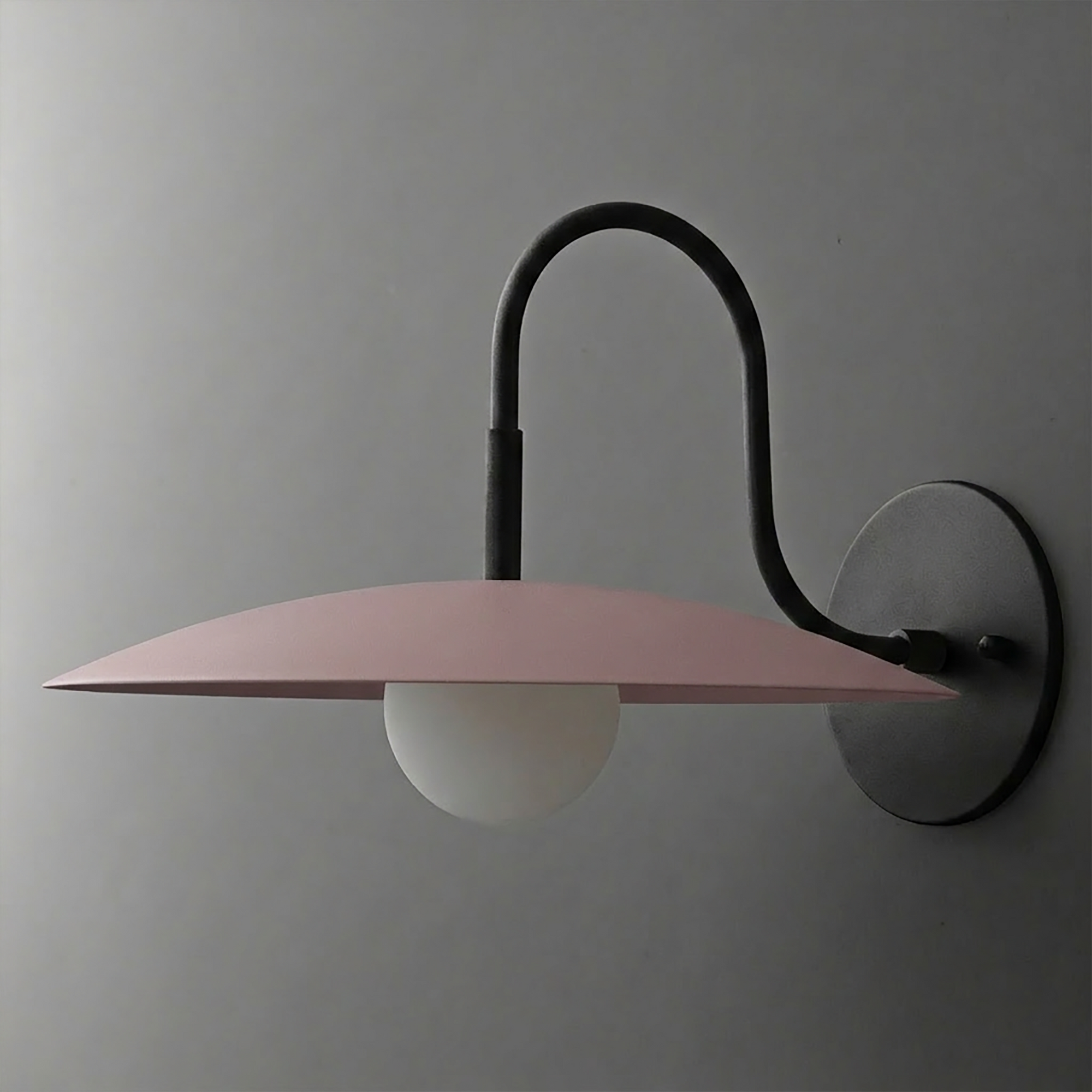 Wall-mounted sconce with curved black arm, matte pink wide disc shade, and white globe bulb. - SCONCE MODEL NO. 9171