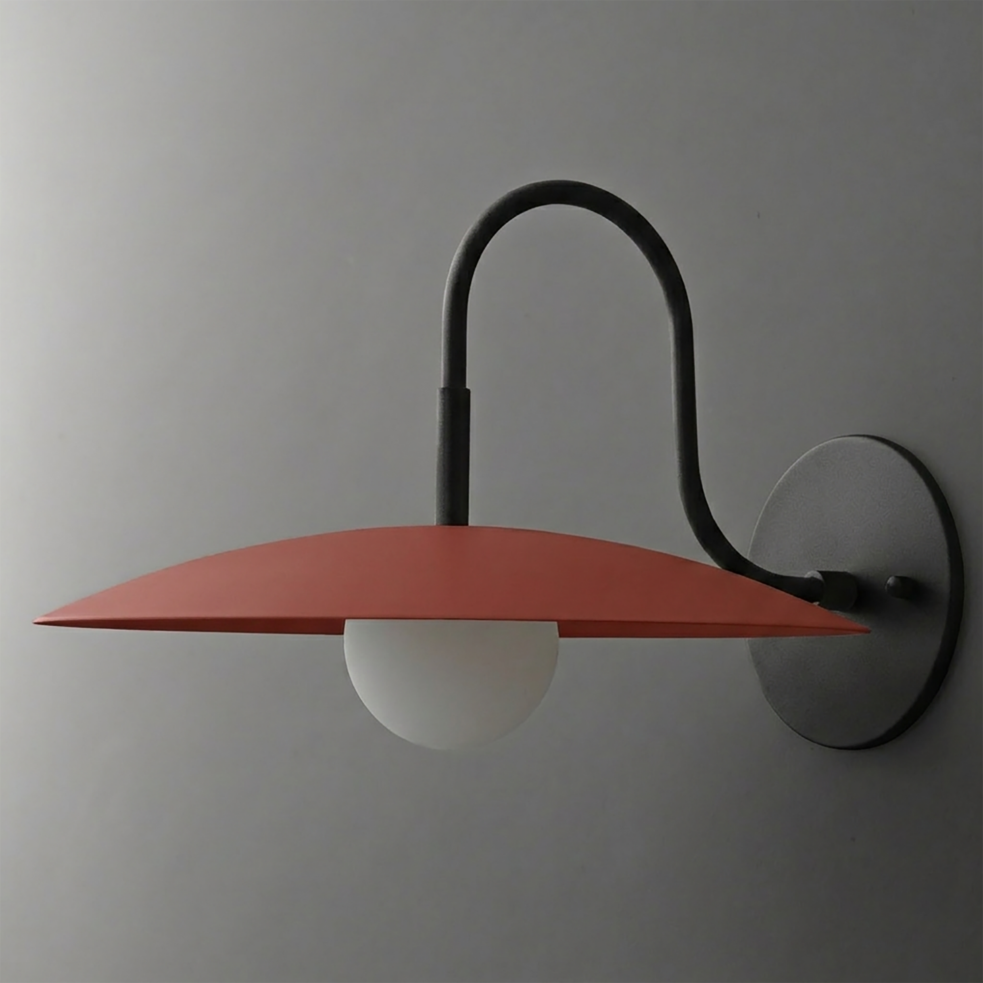 Matte black metal wall sconce with curved arm, rust-colored flat disc shade, and frosted globe bulb. - SCONCE MODEL NO. 9171