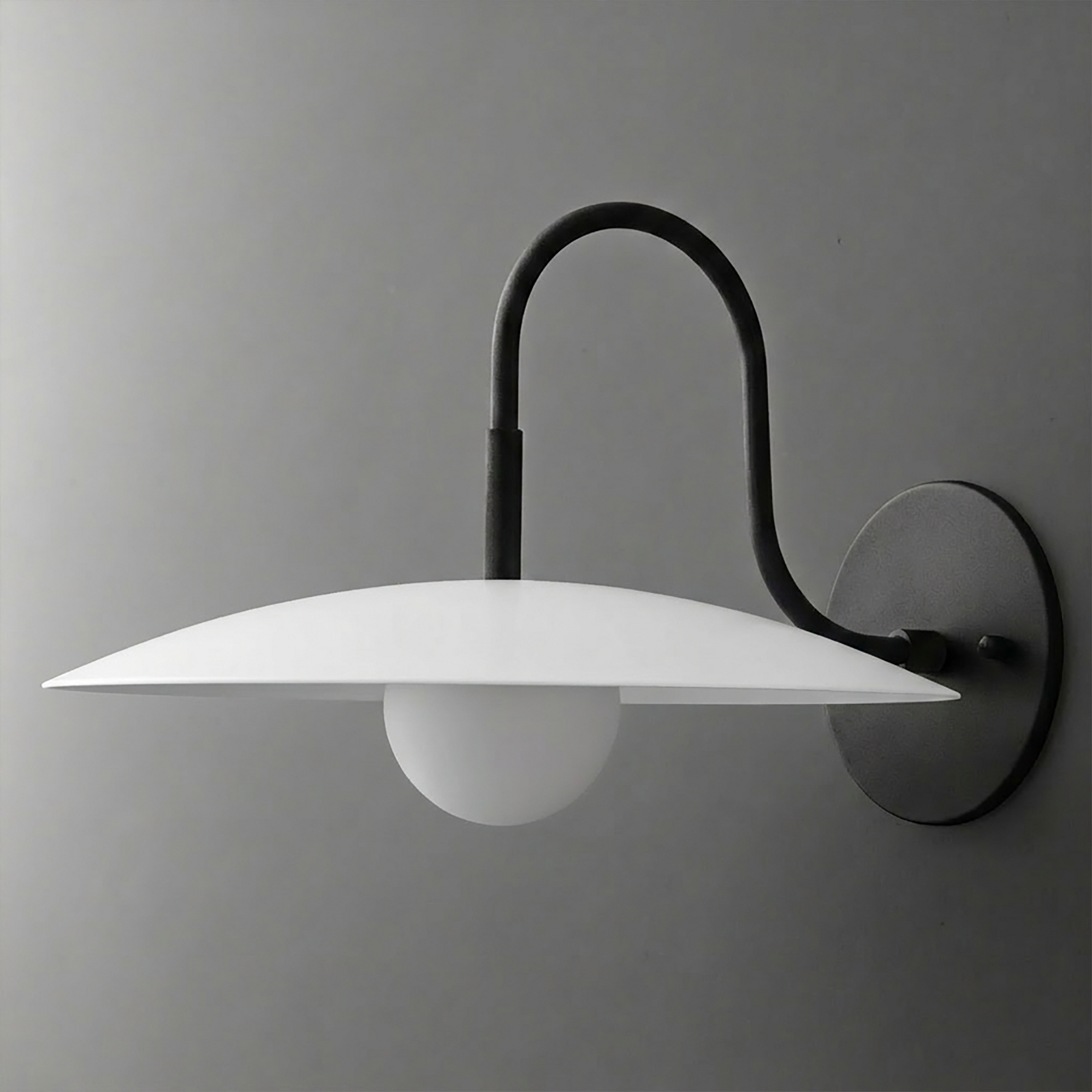 Black metal wall sconce with curved arm, flat white disc shade, and round frosted bulb. - SCONCE MODEL NO. 9171
