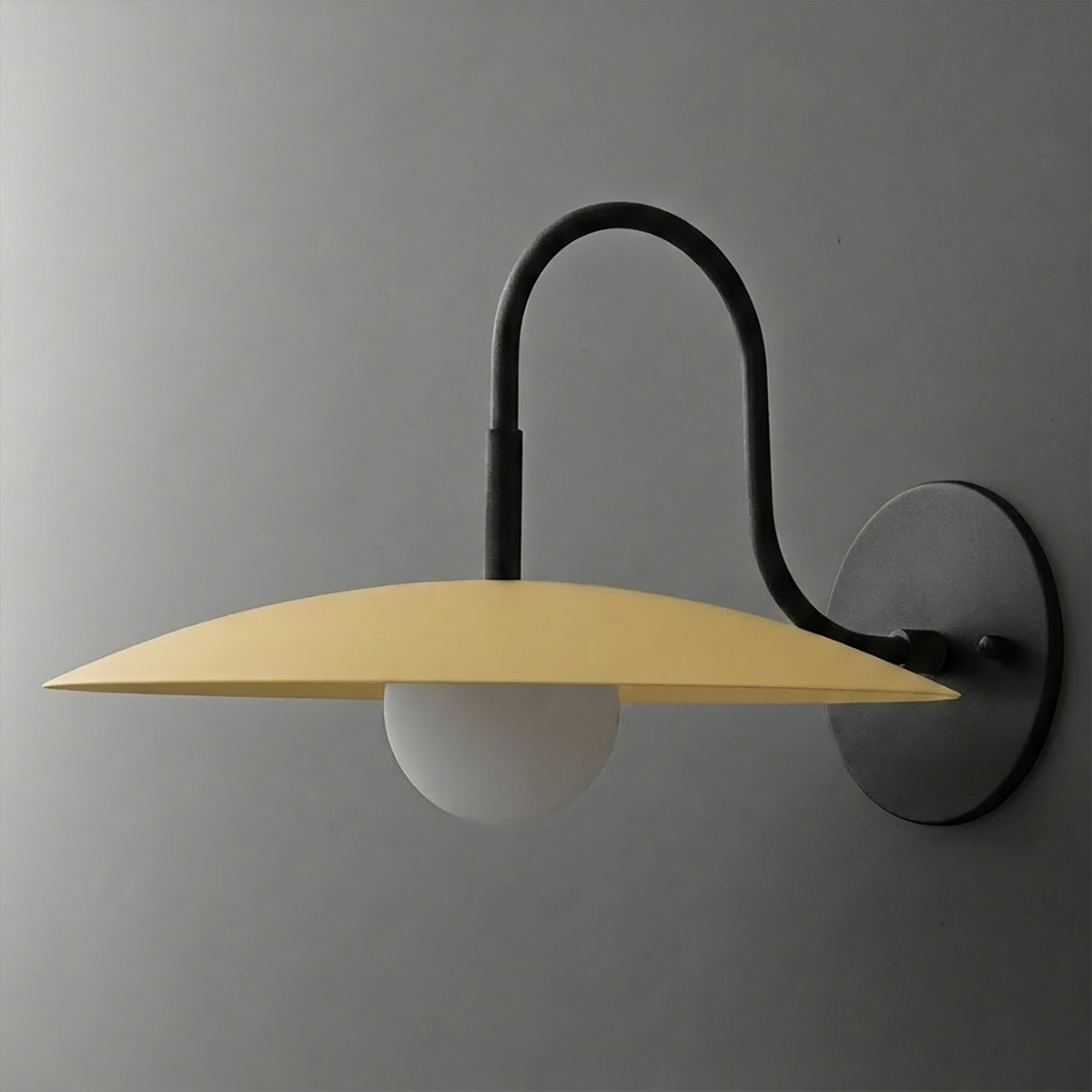 Wall-mounted sconce with matte black curved arm, round base, and wide flat yellow metal shade over frosted globe bulb. - SCONCE MODEL NO. 9171