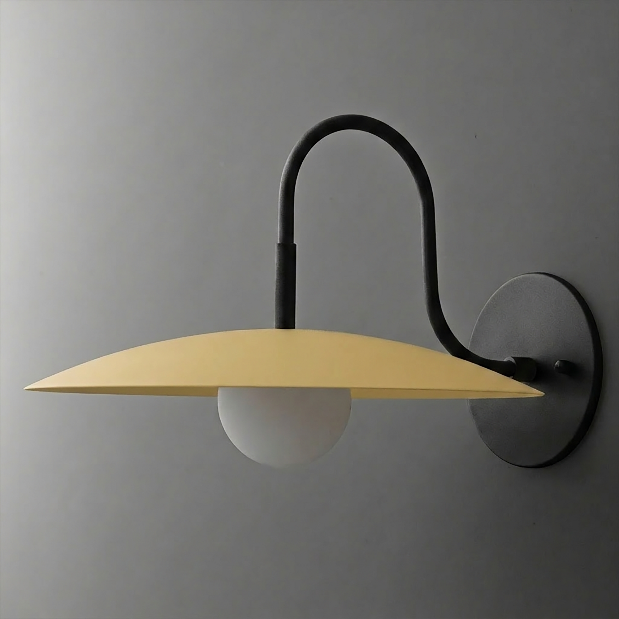 Wall-mounted sconce with matte black curved arm, round base, and wide flat yellow metal shade over frosted globe bulb. - SCONCE MODEL NO. 9171