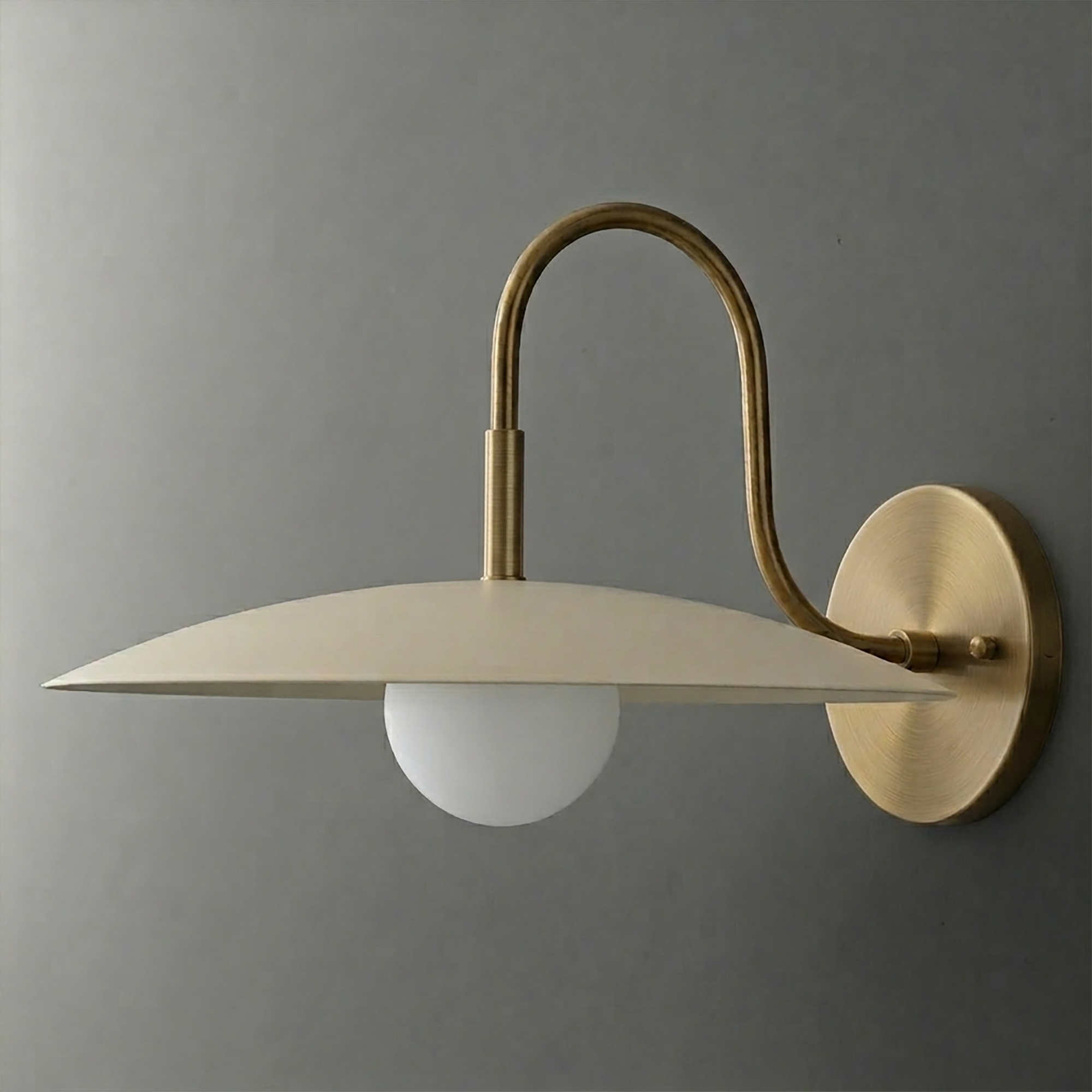 Wall sconce with matte beige dome shade and curved brushed brass arm holding a round white bulb. - SCONCE MODEL NO. 9171