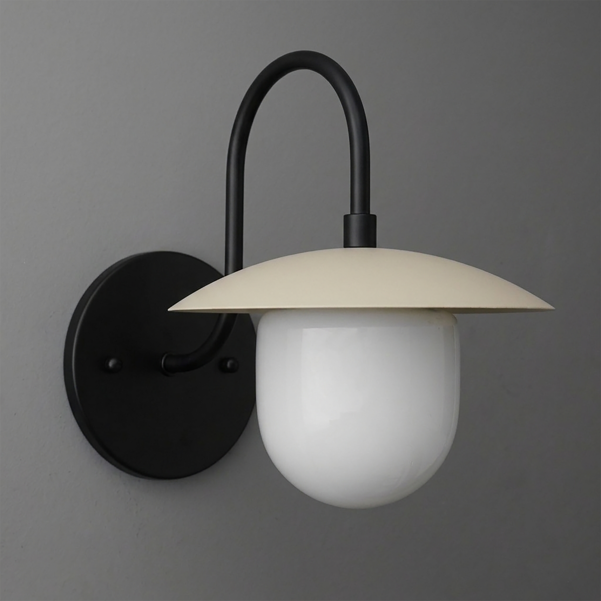 Black metal wall sconce with curved arm, cream flat dome shade, and frosted white glass bulb cover. - SCONCE MODEL NO. 7191