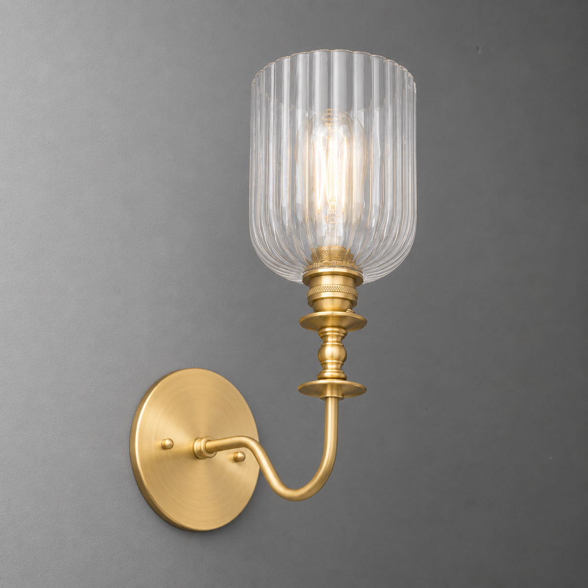 Brushed brass wall sconce with curved arm and ribbed clear glass shade around a single bulb. - SCONCE MODEL NO. 1134