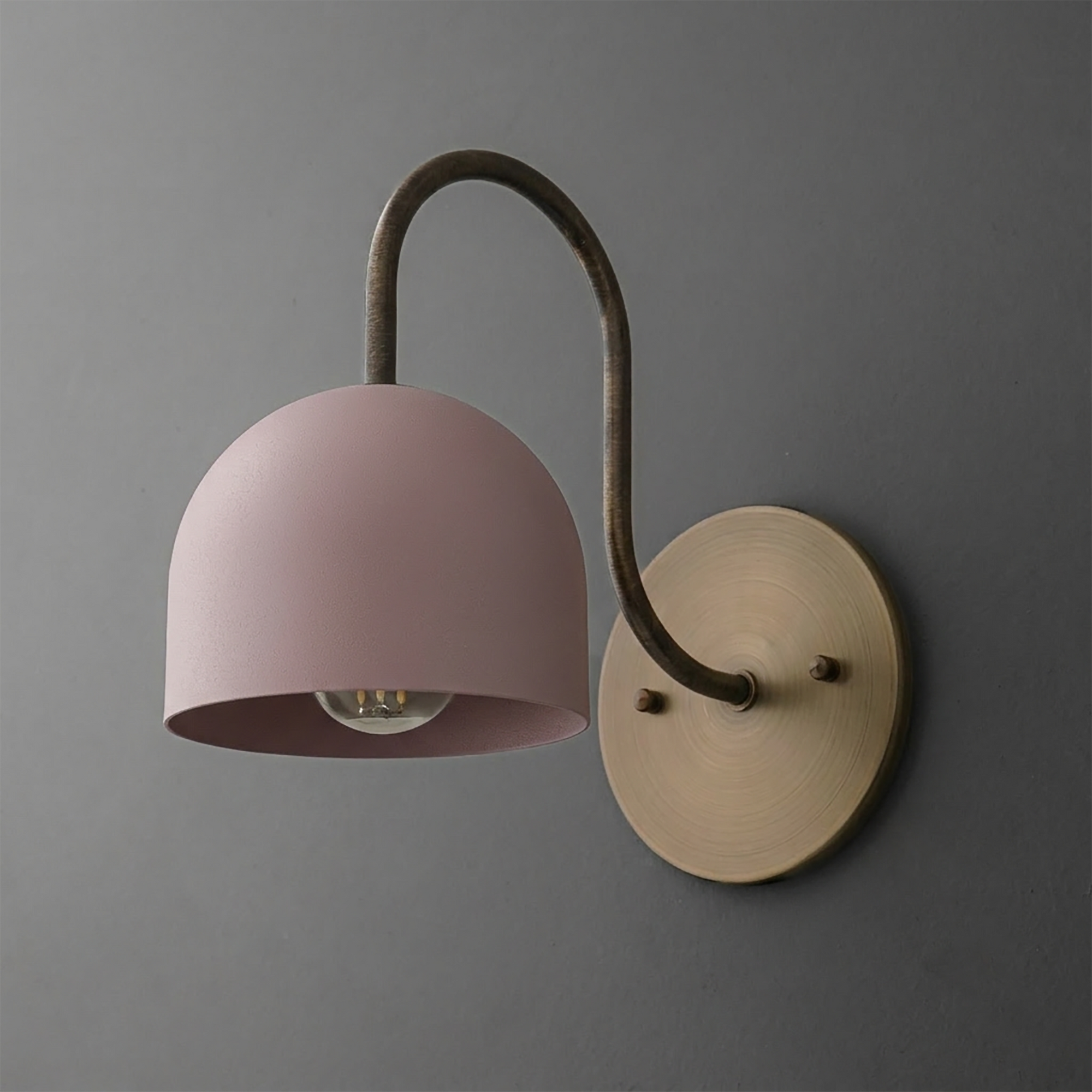 Wall-mounted sconce with a matte pink dome shade, curved dark metal arm, and round brushed brass base. - SCONCE MODEL NO. 6308