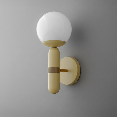 Wall sconce with round white glass globe and vertical cream brass base on gray wall. - SCONCE MODEL NO. 4786