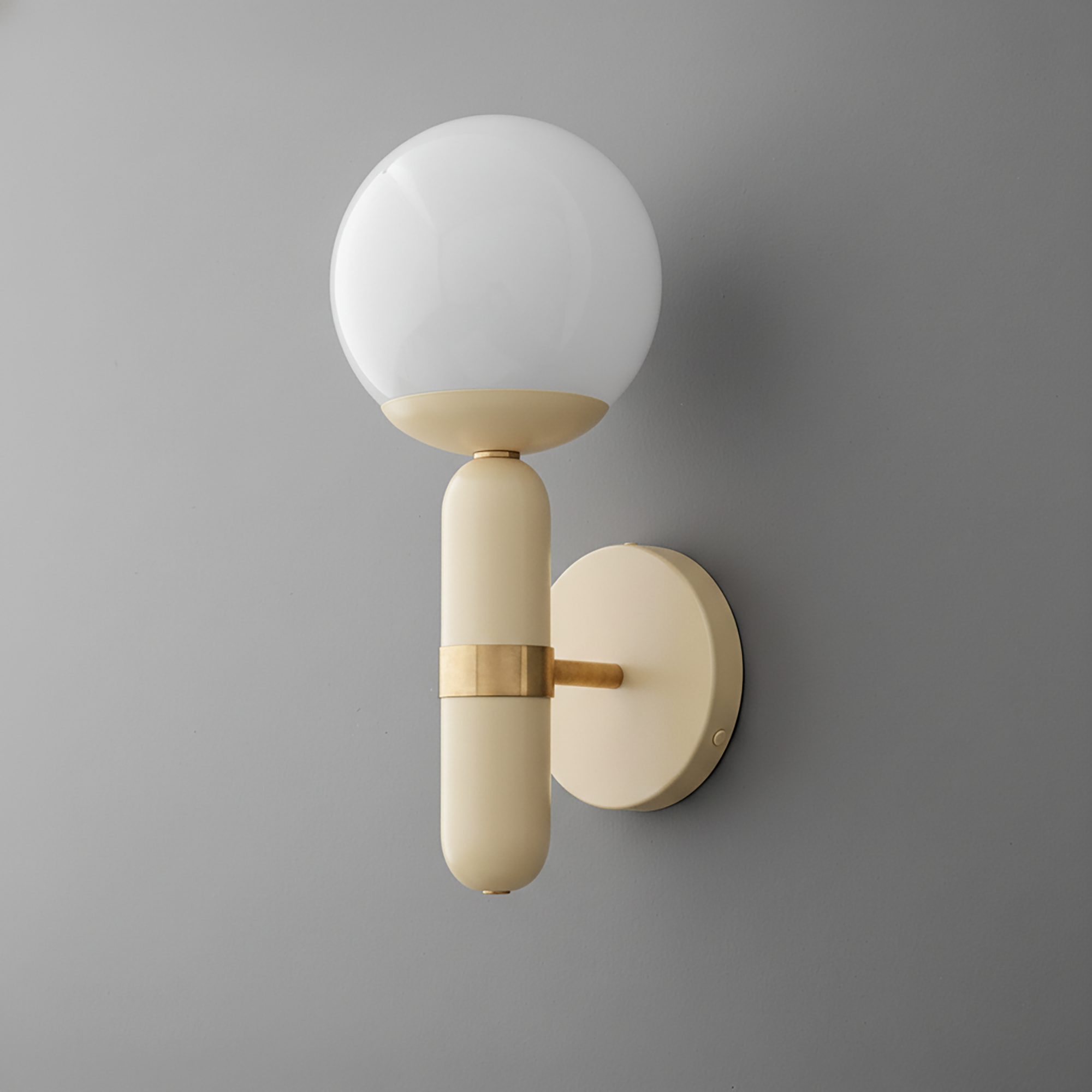 Matte cream cylindrical wall sconce with raw brass accent and round white globe bulb. - SCONCE MODEL NO. 4786