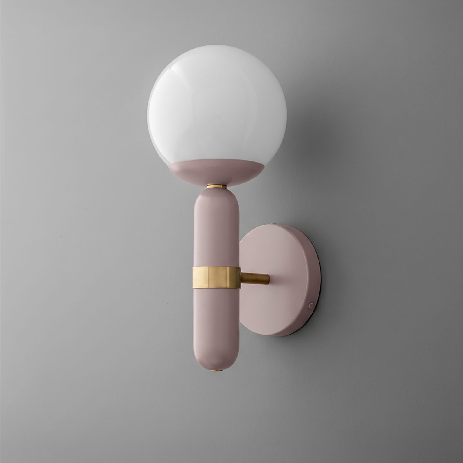 Wall sconce with mauve metal base, raw brass detail, and white round glass shade on gray wall. - SCONCE MODEL NO. 4786