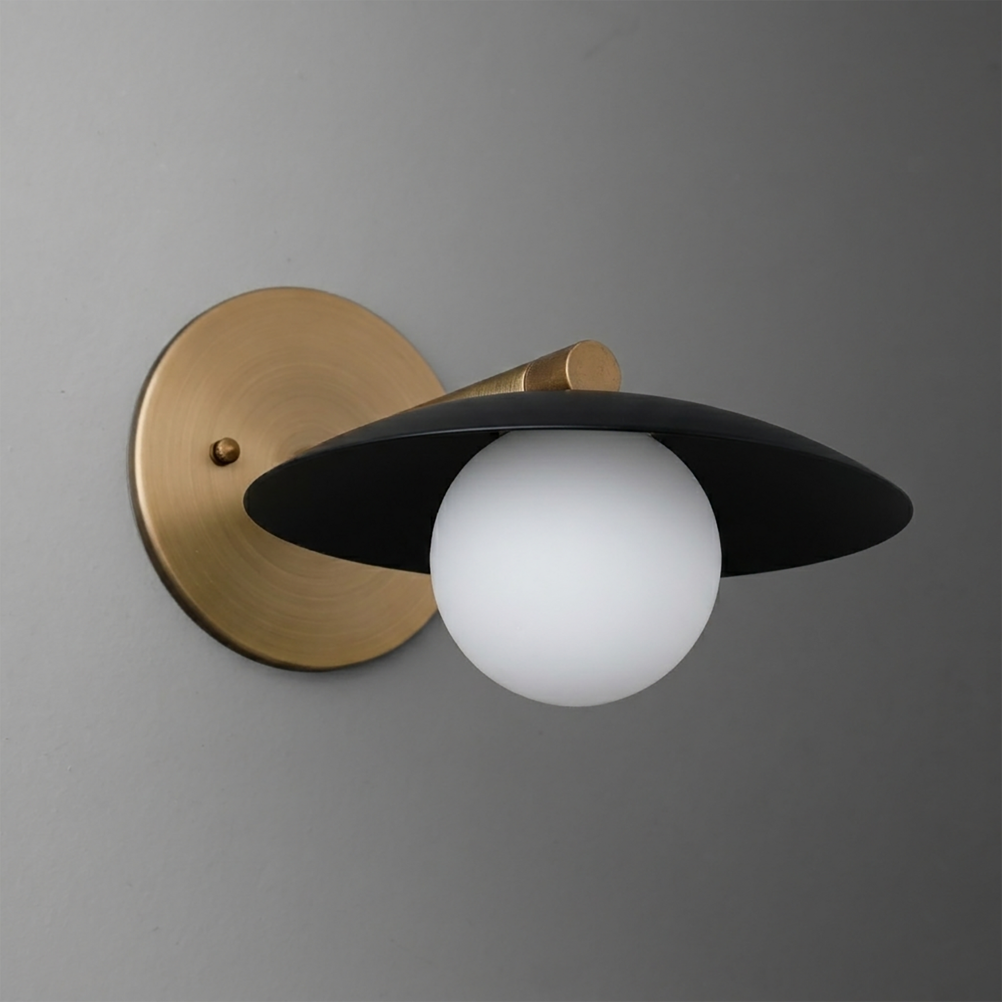 Wall sconce with matte black wide metal shade, white globe bulb, and brushed brass round base. - SCONCE MODEL NO. 9872