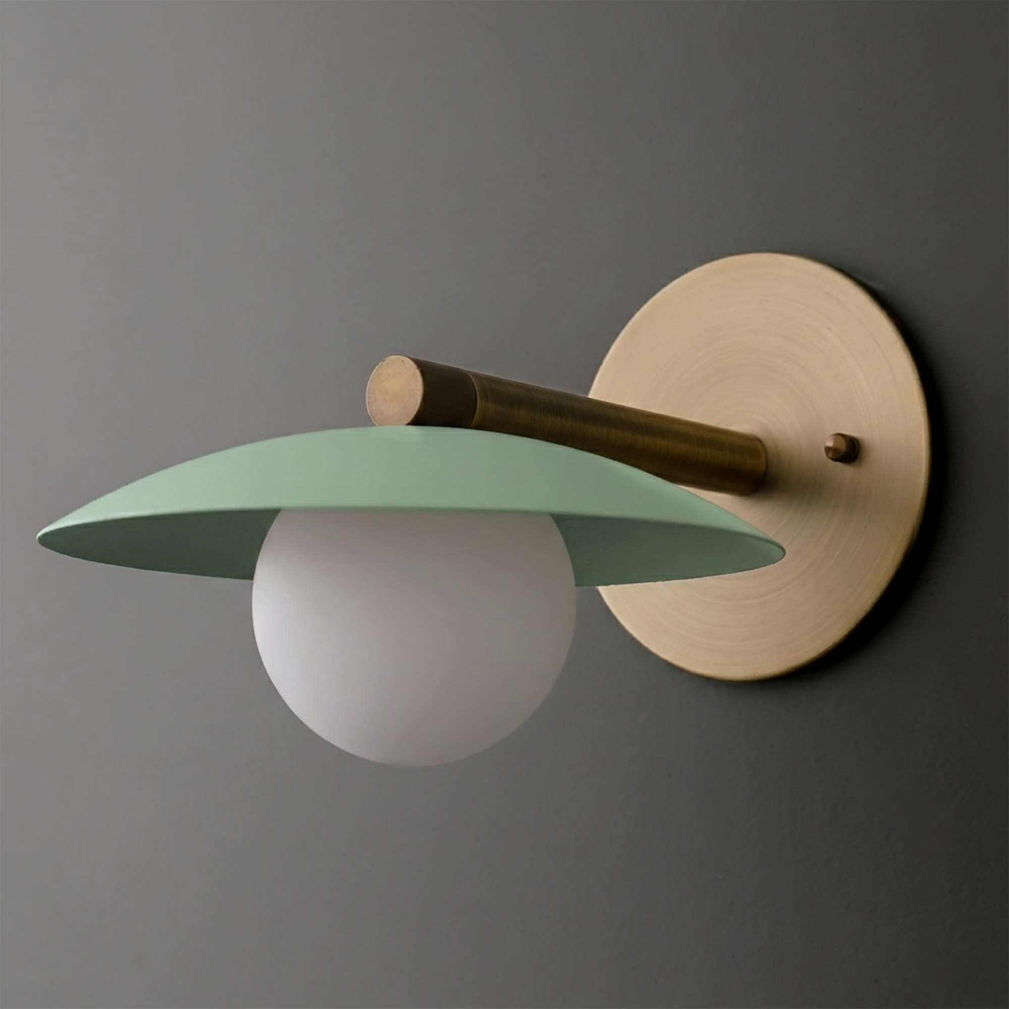 Wall sconce with matte green flat dome shade, frosted white globe bulb, and brass circular mount. - SCONCE MODEL NO. 9872