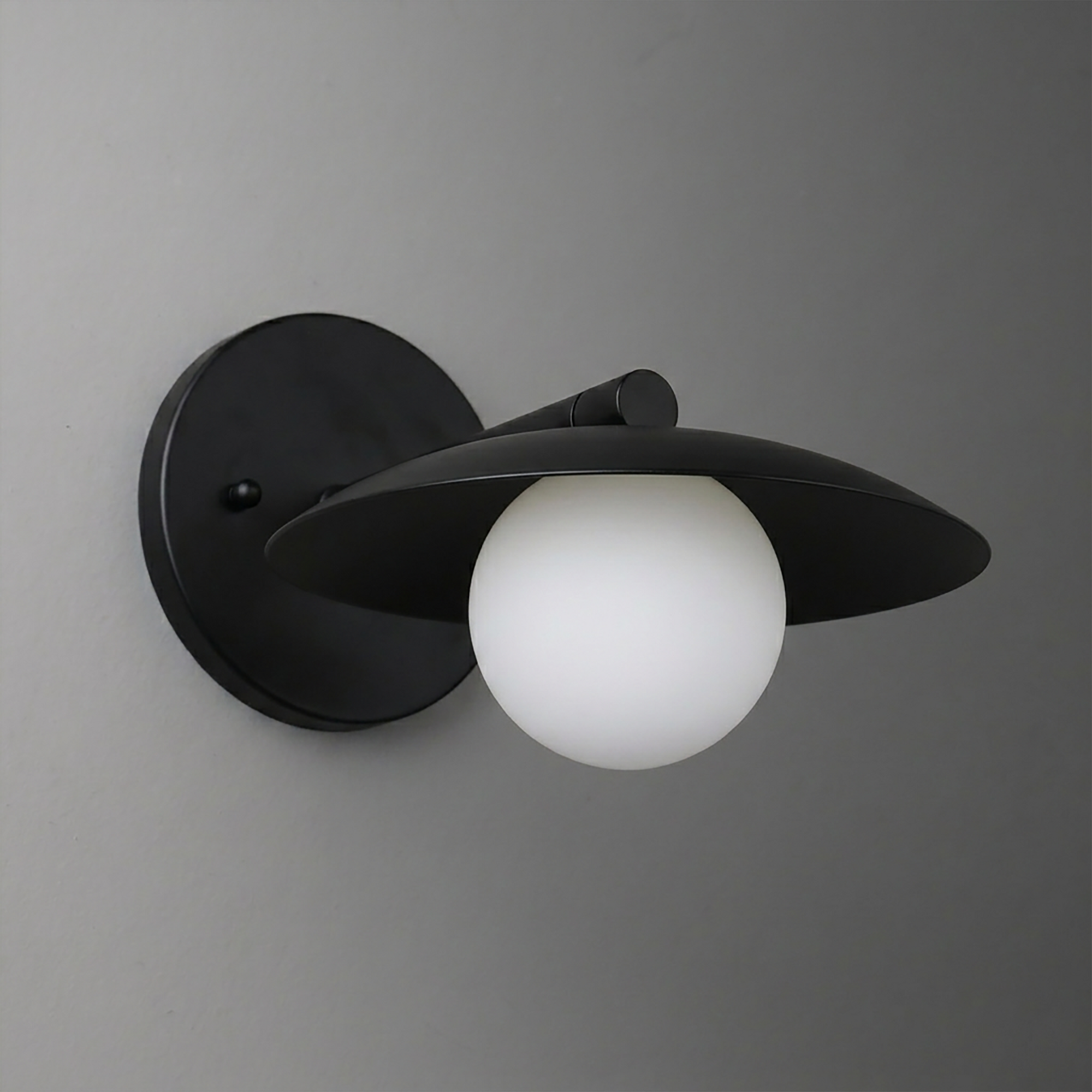 Black metal wall sconce with a wide disk-shaped shade and a white frosted glass globe bulb. - SCONCE MODEL NO. 9872