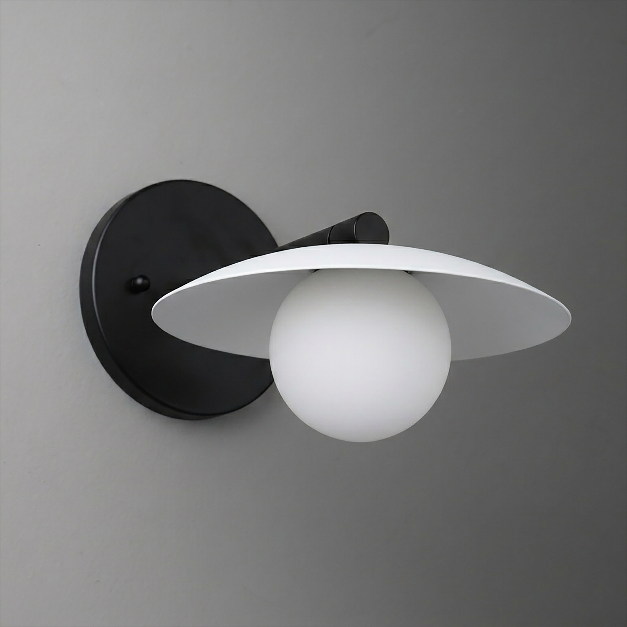 Black metal wall sconce with a white globe bulb and flat circular shade. - SCONCE MODEL NO. 9872