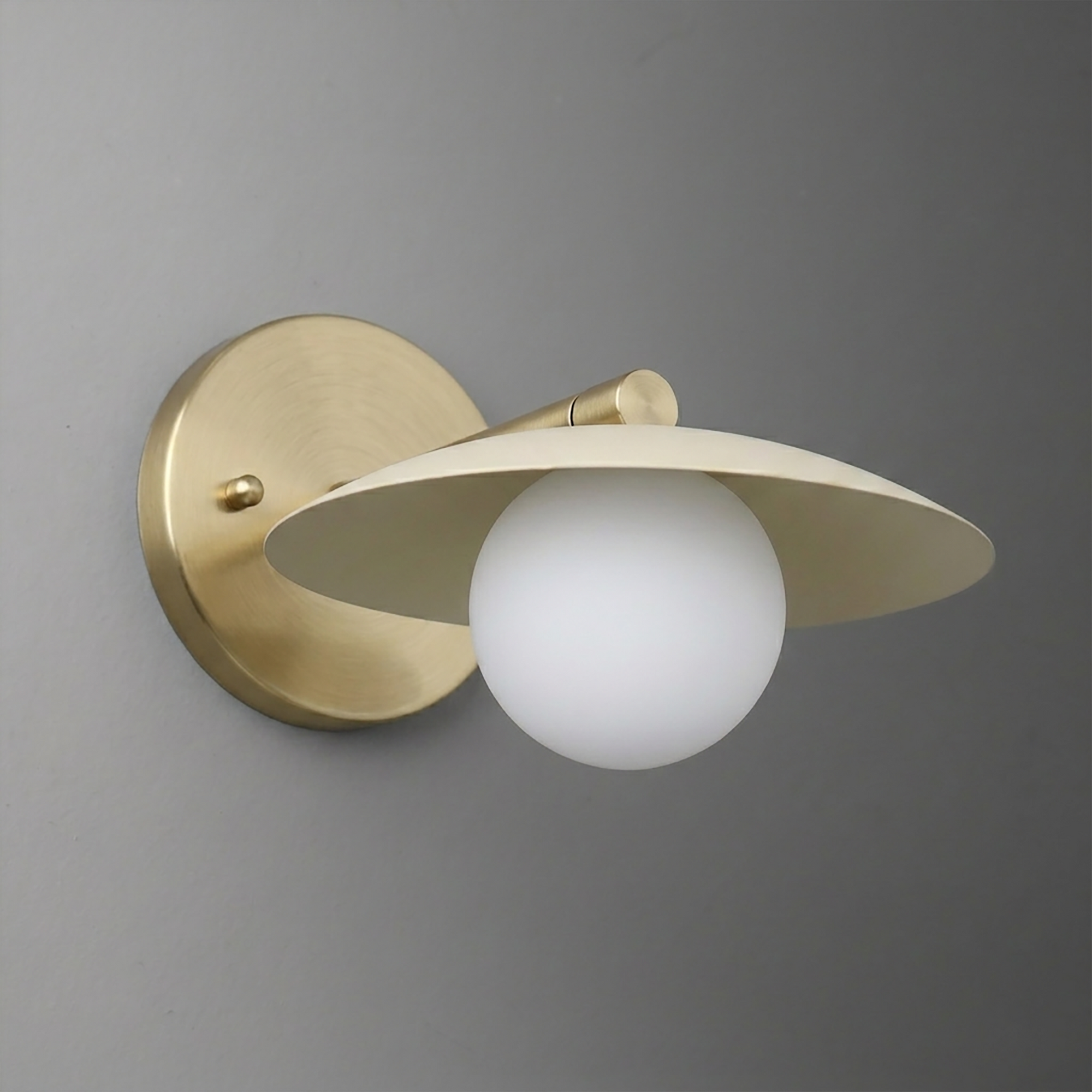 Matte brass wall sconce with a round backplate, angled flat metal shade, and white globe bulb. - SCONCE MODEL NO. 9872