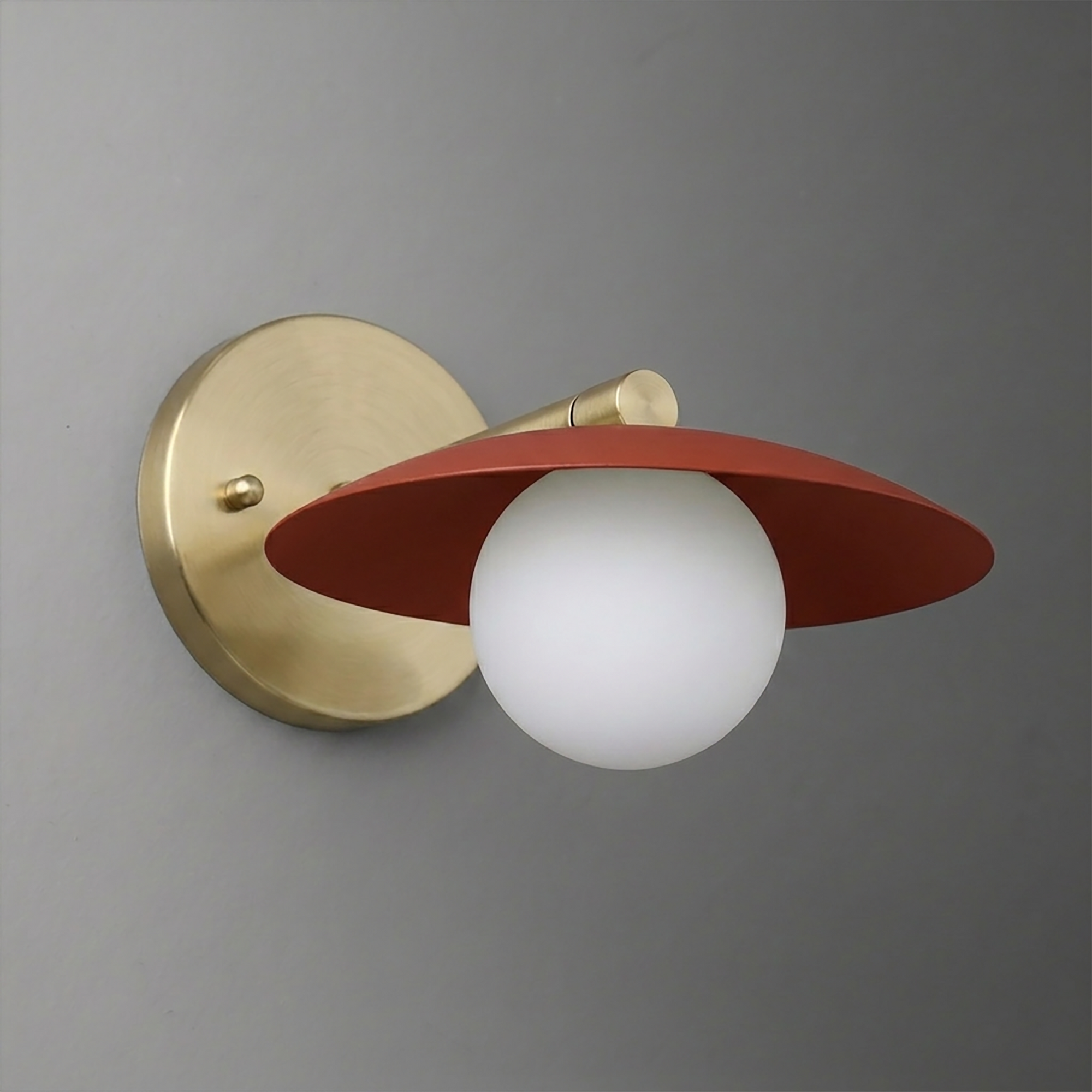 Wall sconce with matte gold circular base, white globe bulb, and flat rust-red shade angled downward. - SCONCE MODEL NO. 9872