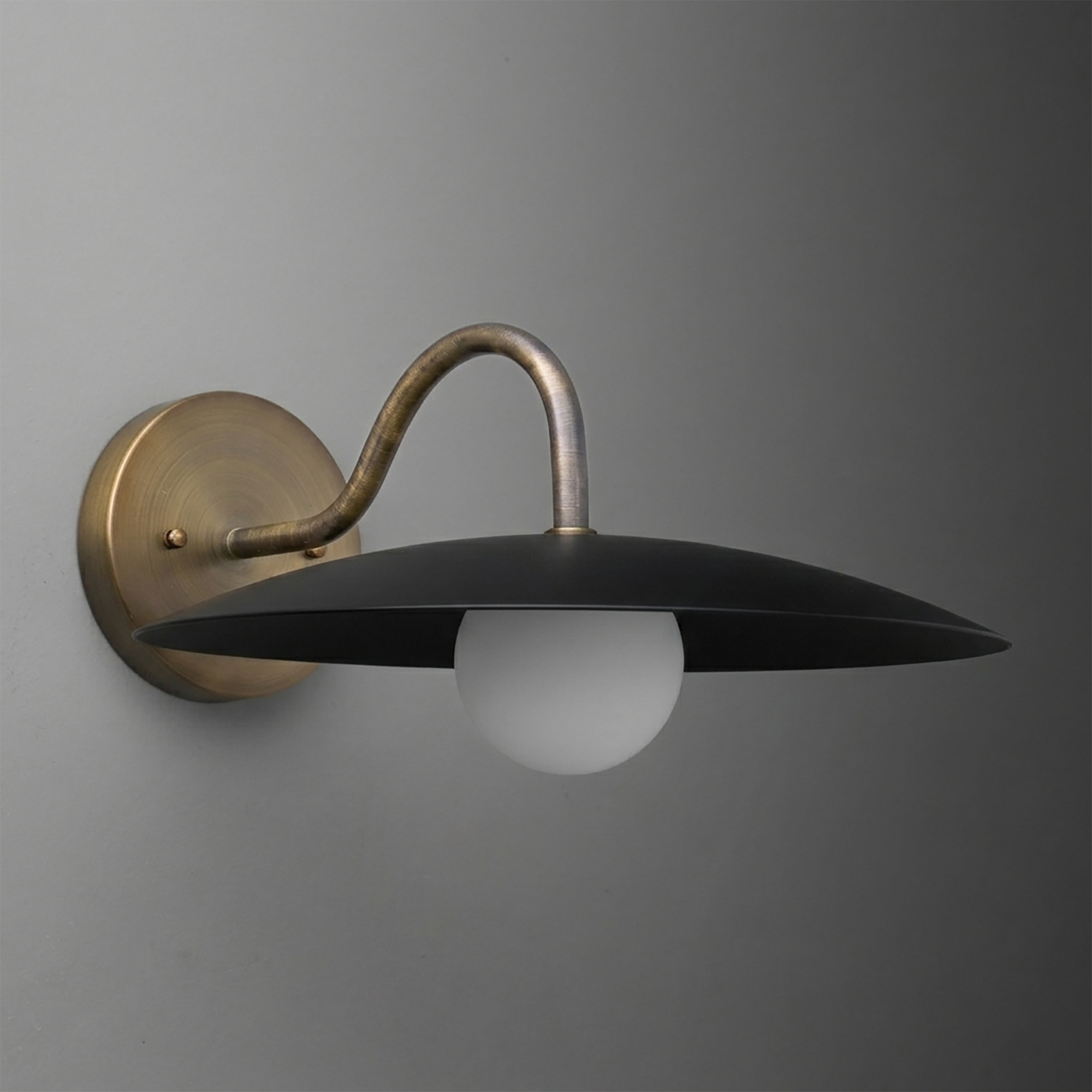 Wall-mounted sconce with a curved brass arm and wide black metal shade covering the bulb. - SCONCE MODEL NO. 2162