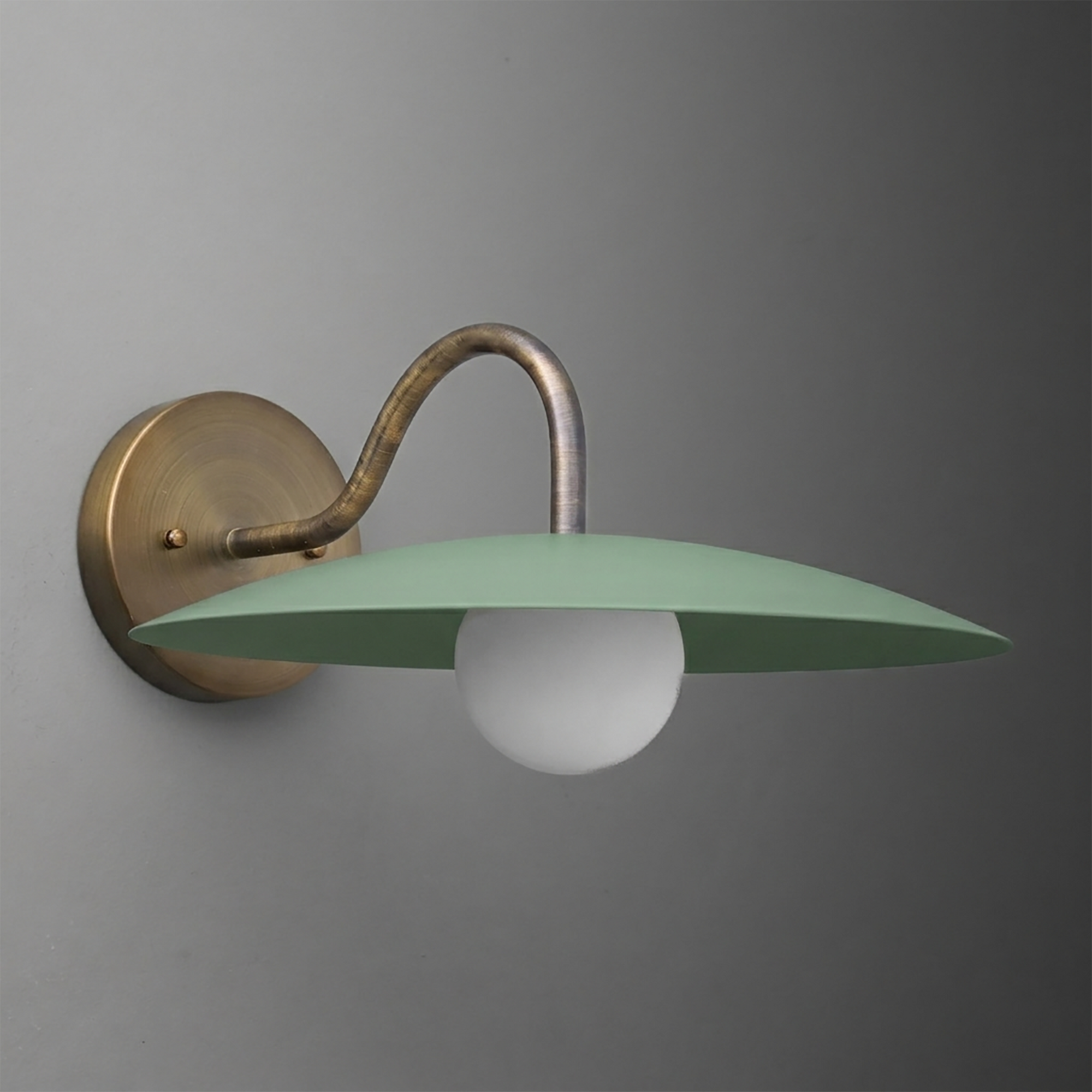 Wall sconce with aged brass circular base and arm, featuring a wide flat green metal shade and exposed white bulb. - SCONCE MODEL NO. 2162