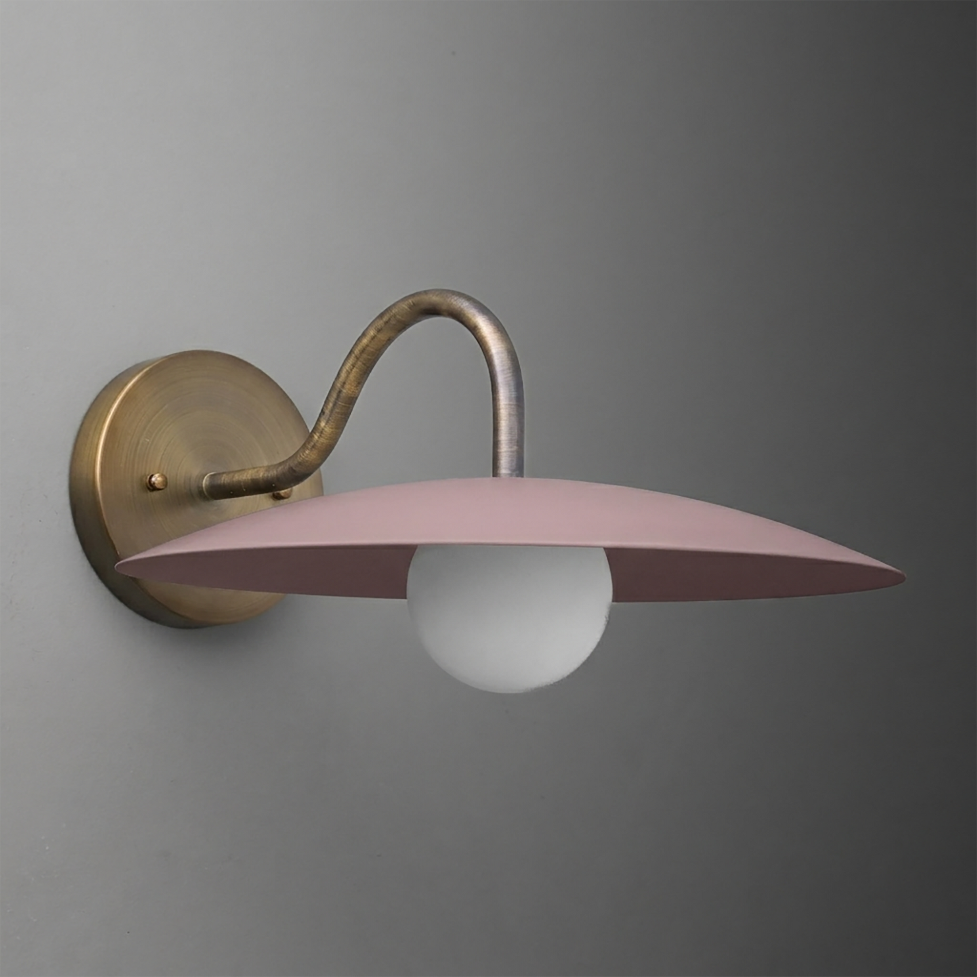 Wall-mounted sconce with aged brass curved arm and round base, featuring a matte pink wide, flat shade and a single exposed. - SCONCE MODEL NO. 2162