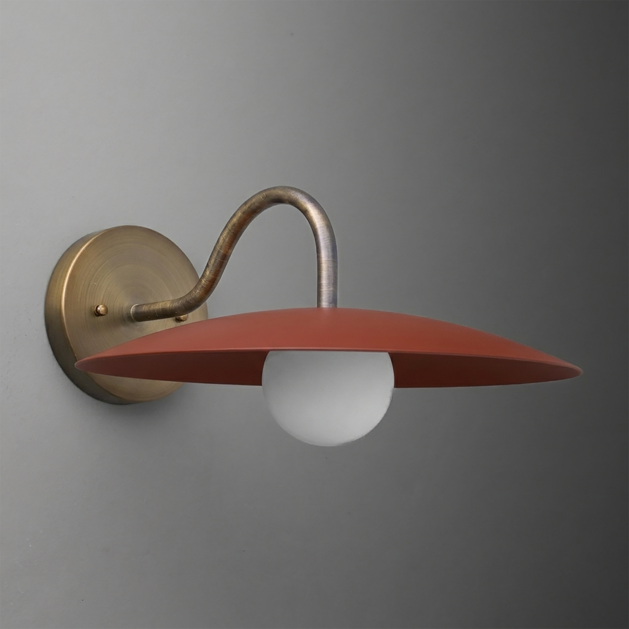 Wall sconce with a curved brass arm and a flat, wide red metal shade covering a round white bulb. - SCONCE MODEL NO. 2162