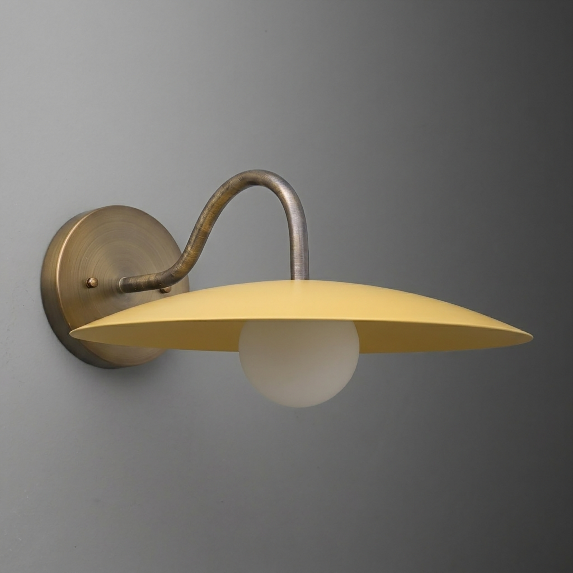Wall-mounted sconce with a curved antique brass arm and a flat, wide mustard yellow metal shade over a white globe bulb. - SCONCE MODEL NO. 2162