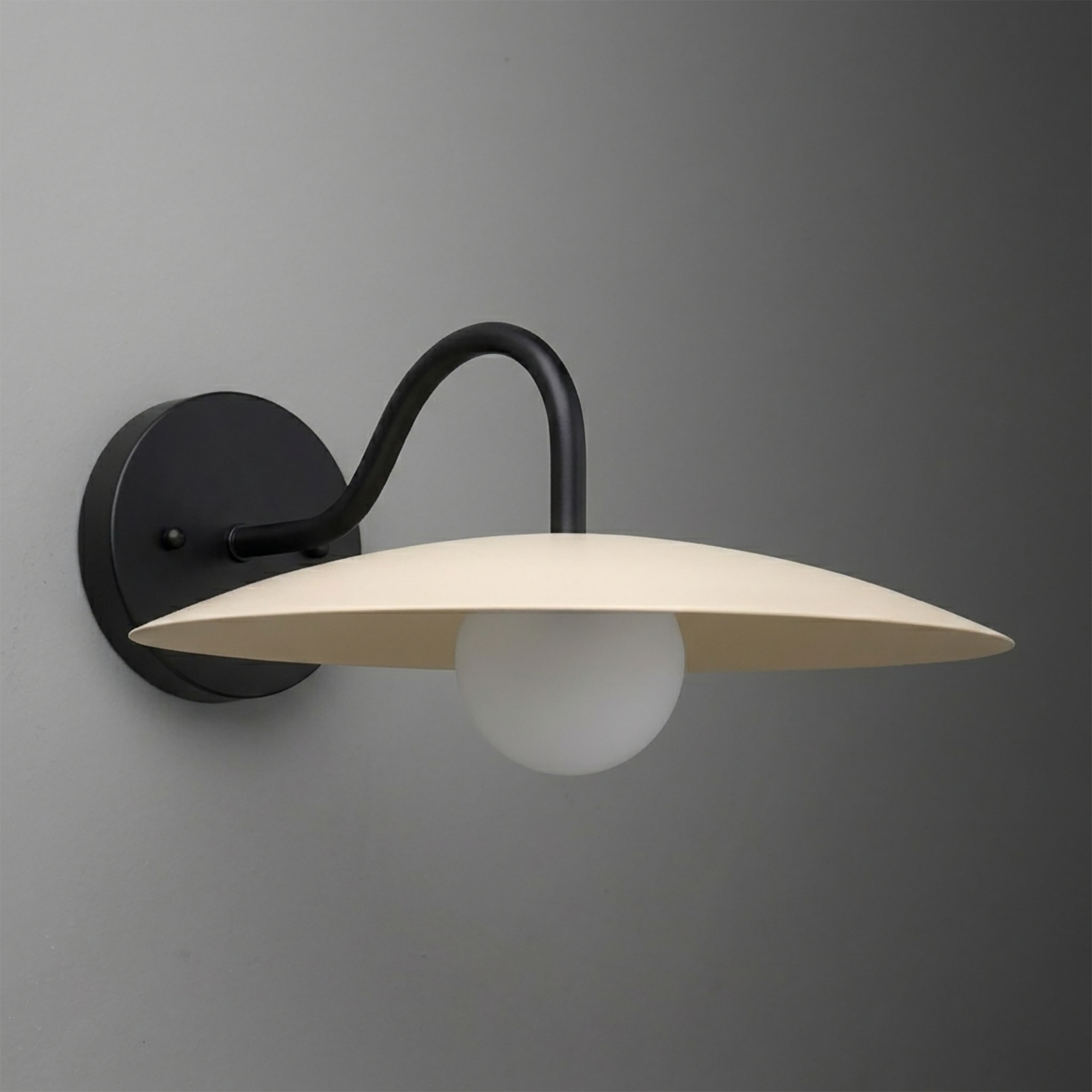 Matte black metal wall sconce with curved arm and wide cream-colored flat shade over frosted white globe bulb. - SCONCE MODEL NO. 2162