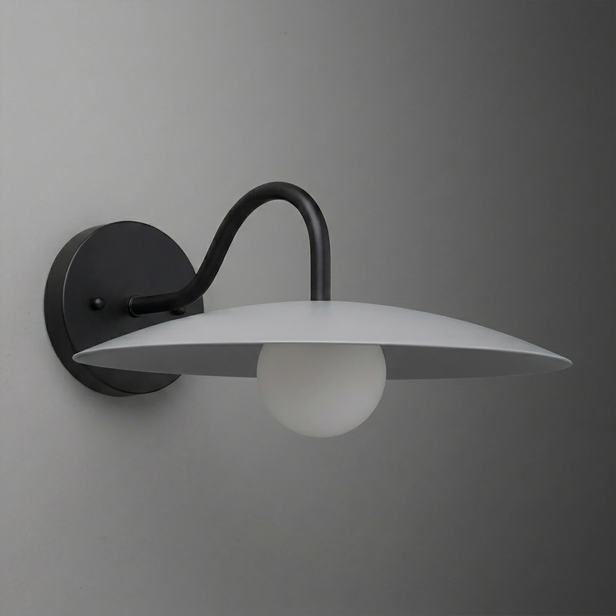 Wall-mounted sconce with matte black curved arm and round base, featuring a flat, wide white shade and a frosted globe bulb. - SCONCE MODEL NO. 2162