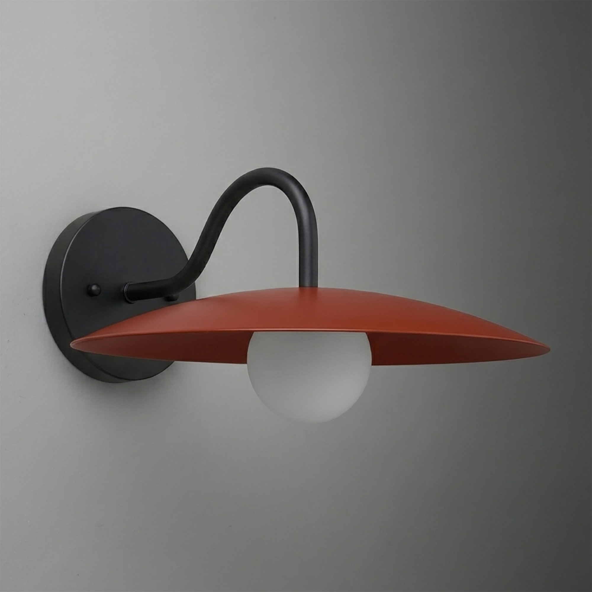 Wall sconce with matte black curved arm and round red-orange flat metal shade over frosted white bulb. - SCONCE MODEL NO. 2162