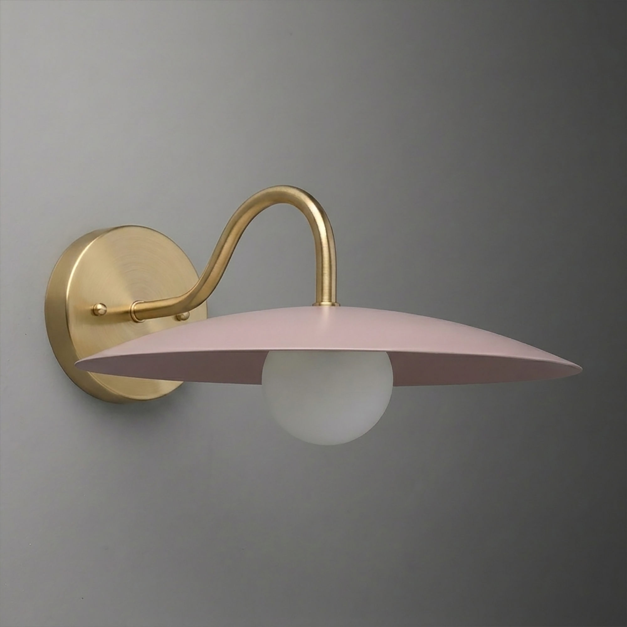 Wall-mounted sconce with a curved brass arm, round brass base, and flat pink metal shade above a white globe bulb. - SCONCE MODEL NO. 2162