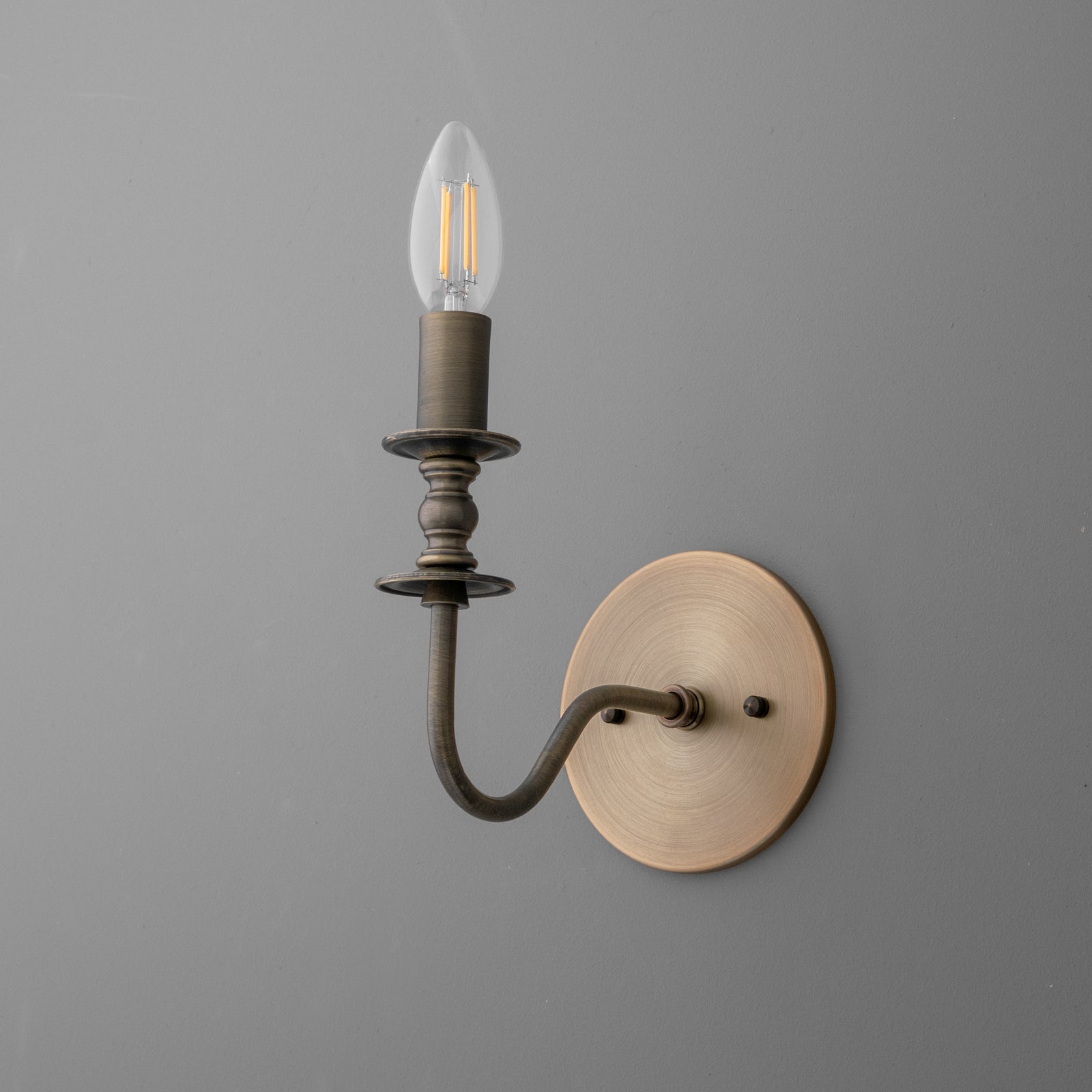 Antique bronze wall sconce with curved arm and exposed bulb on round backplate. - SCONCE MODEL NO. 9915