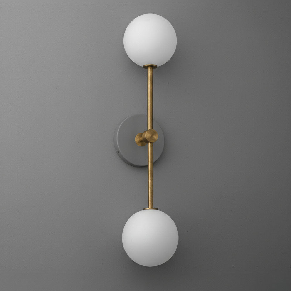Modern double globe wall sconce with raw brass finish and frosted white glass shades on gray background. - SCONCE MODEL NO. 9776